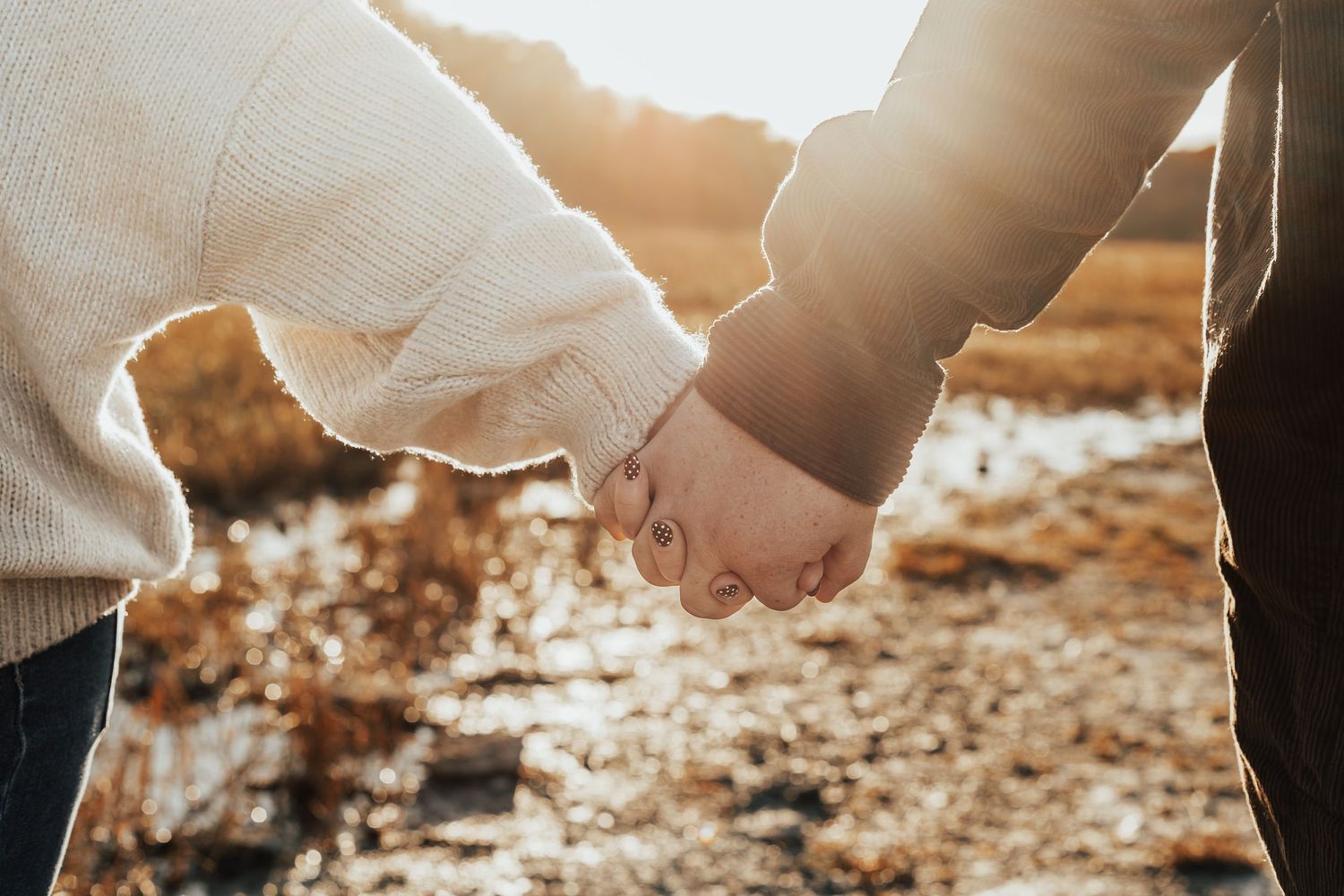 Close-up of couple holding hands in warm sunlight with textured ground beneath.
