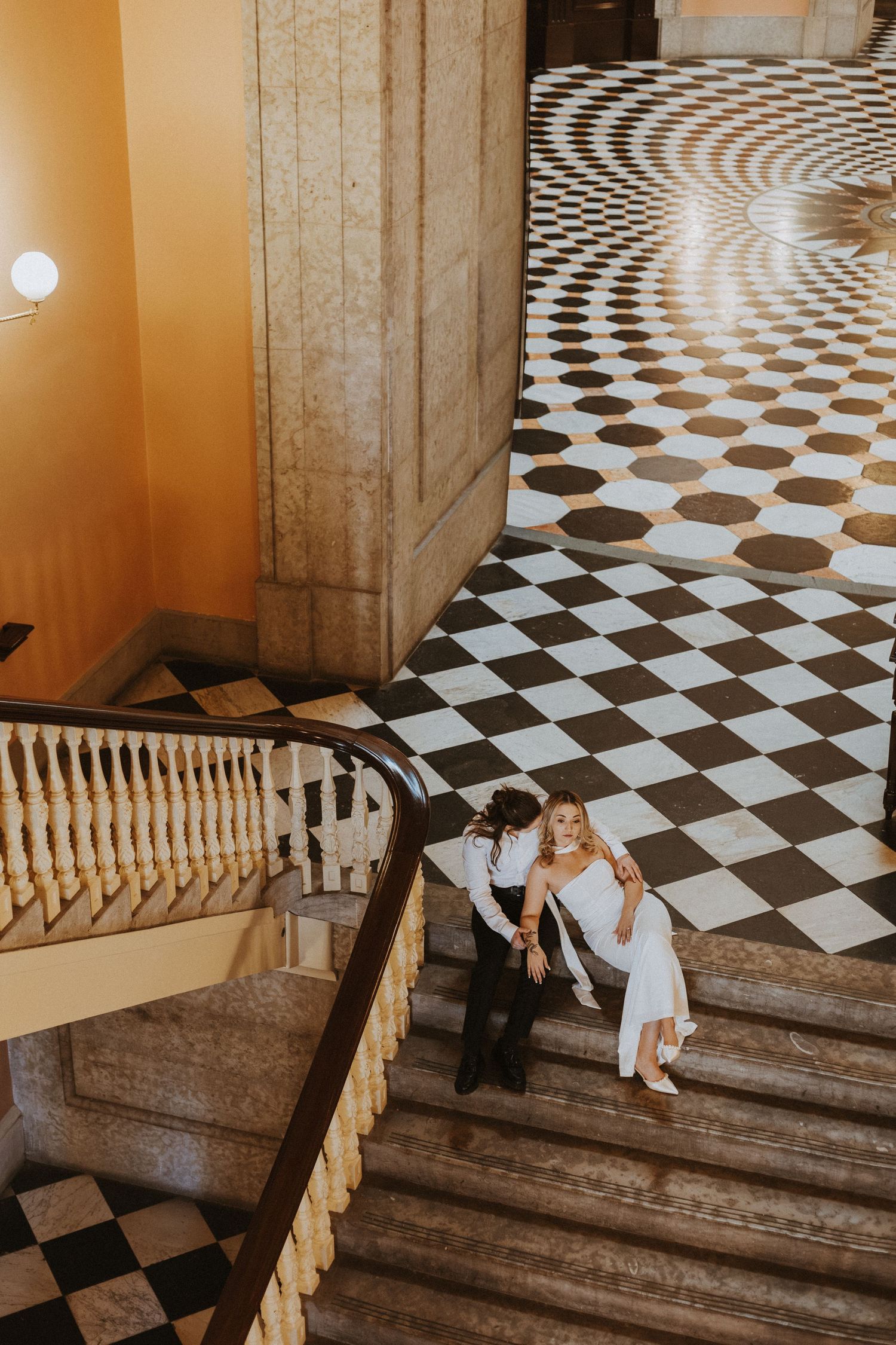 Couple in wedding attire on grand marble staircase with stunning black and white checkered floor pattern.