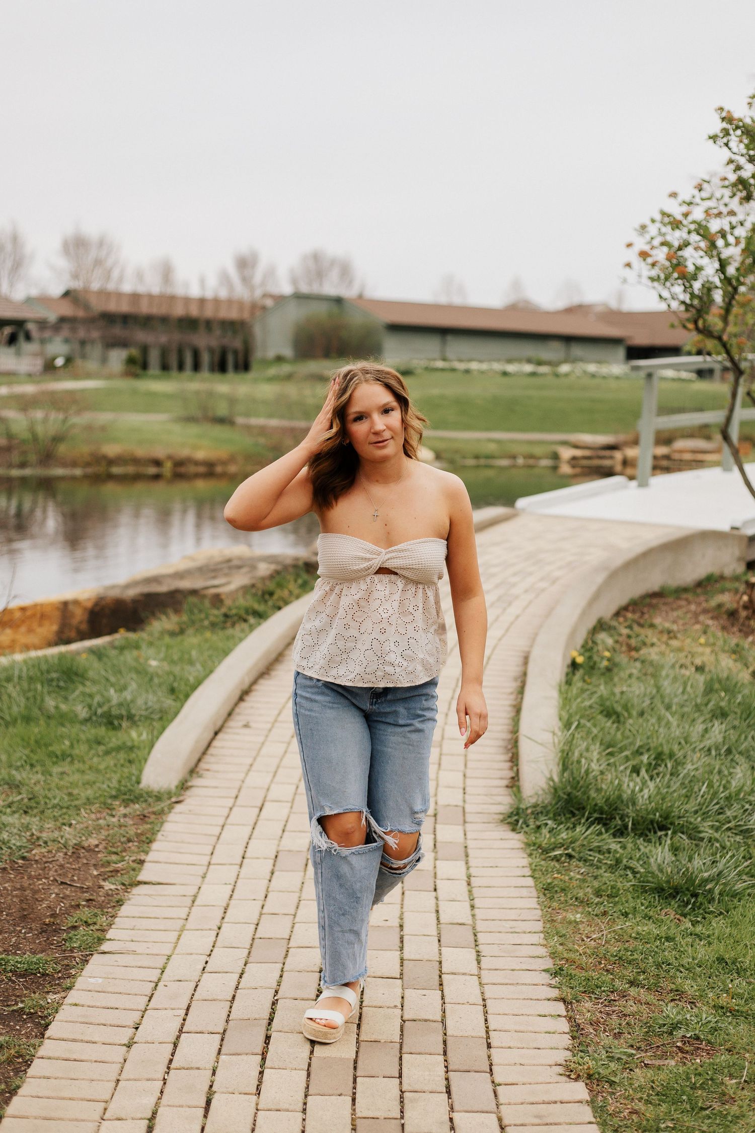 A person walks and poses along a curved brick pathway through a grassy landscape.