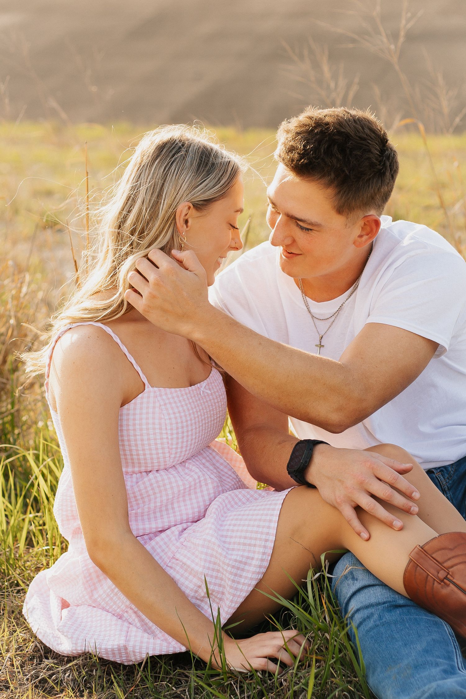 Romantic couple sitting in tall grass during golden hour sharing an intimate moment.