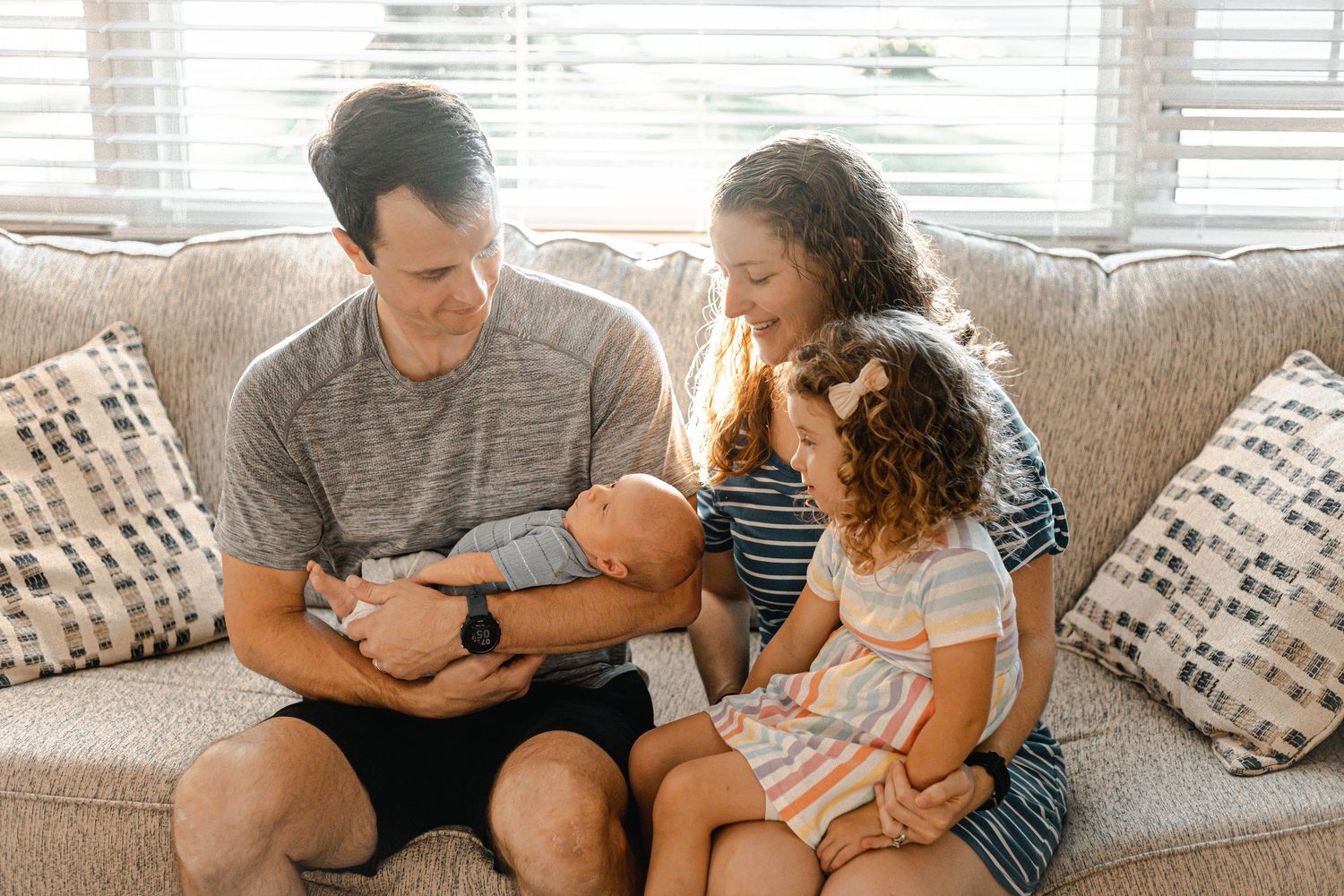 Family relaxing together on grey couch in living room with natural lighting.