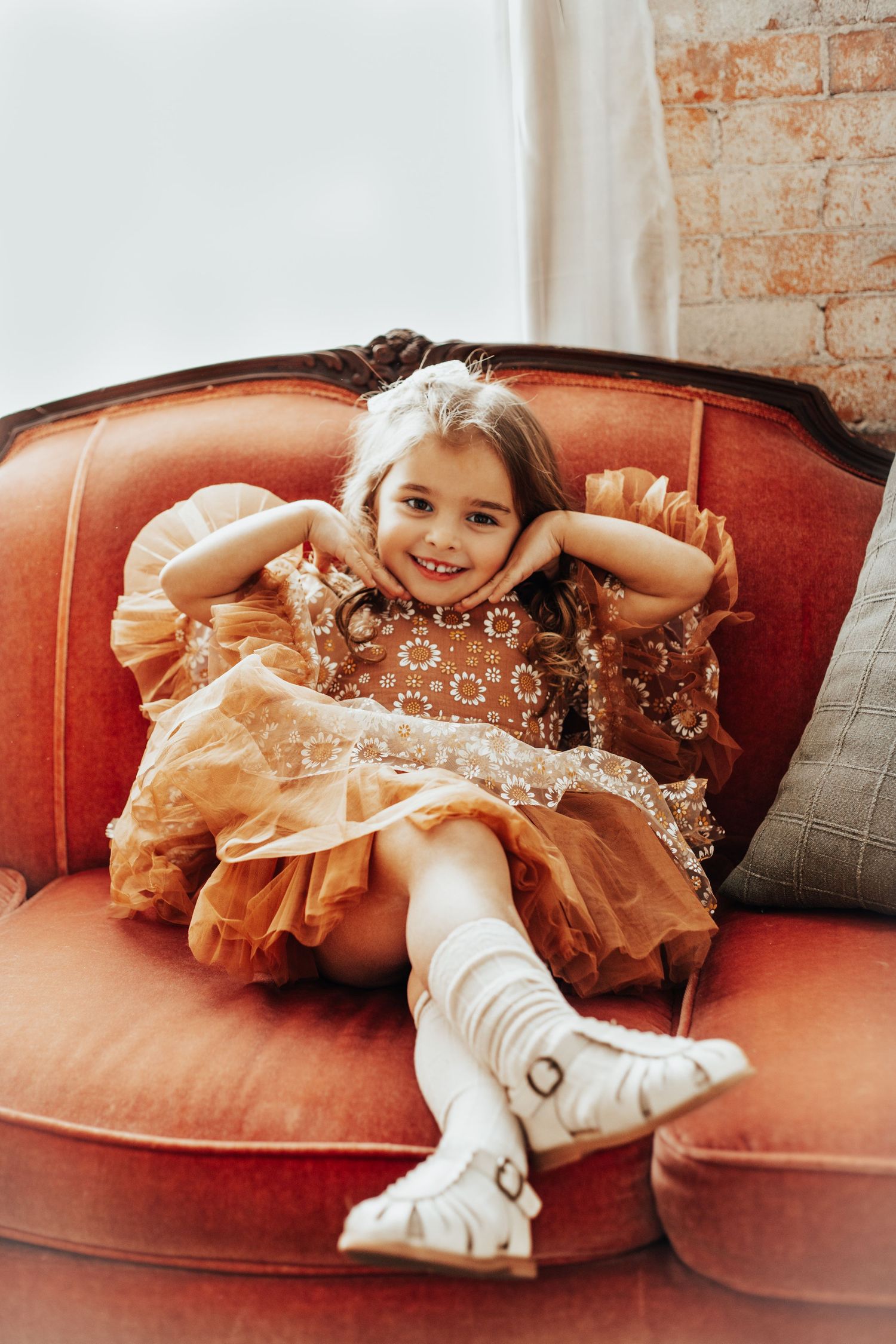 Child in a glittery dress poses playfully on a vintage red couch.
