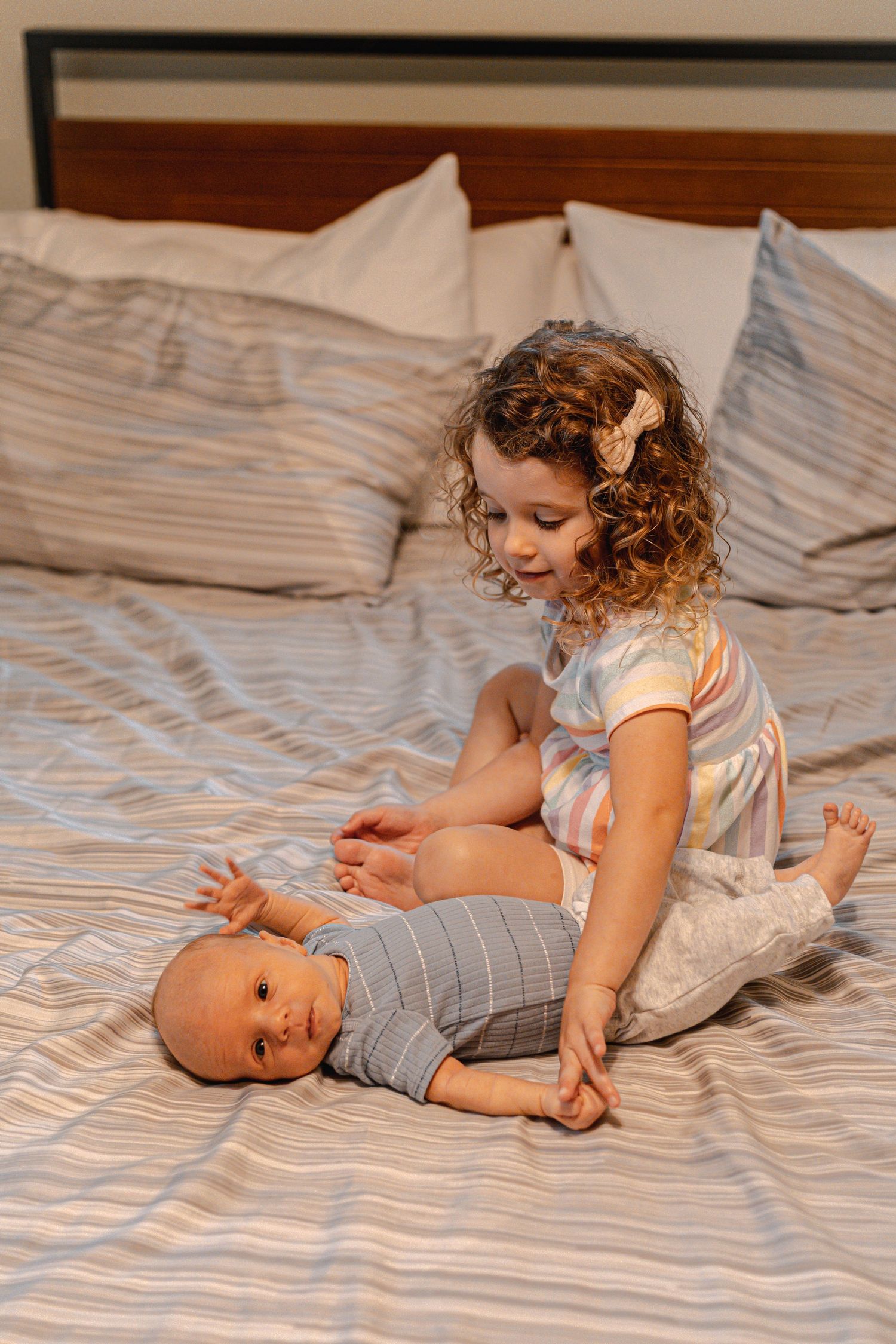Siblings bonding on a bed as older child interacts with baby.