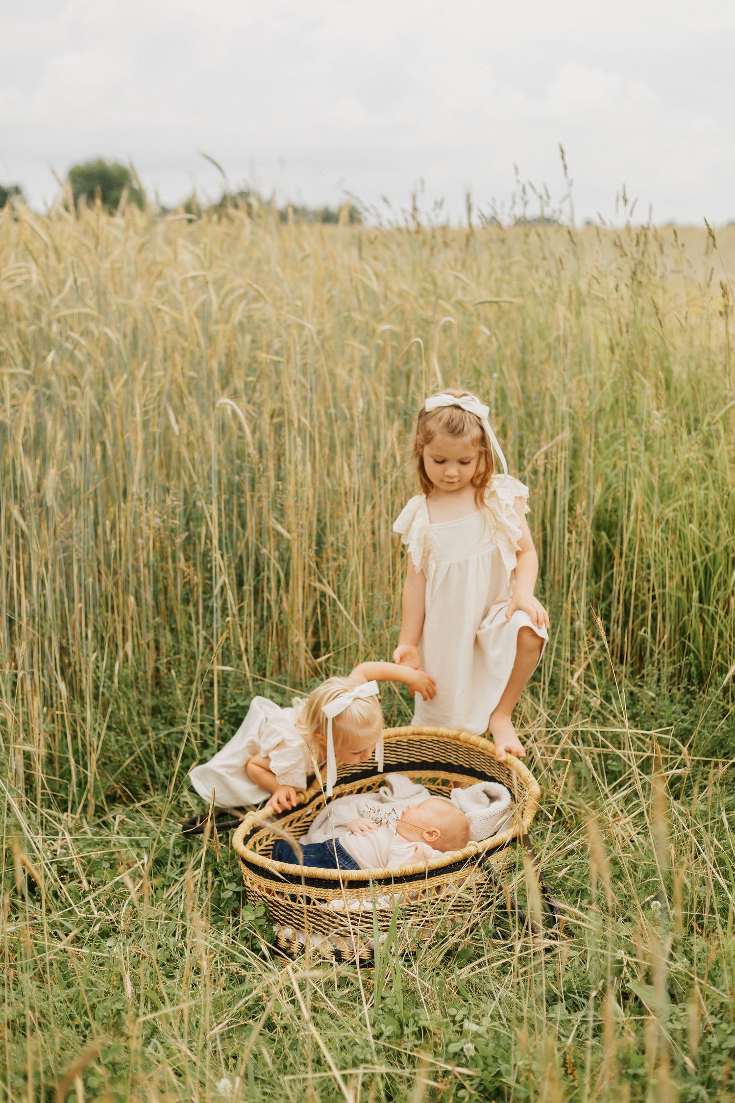 Child sitting by woven basket in tall grass field during golden hour.