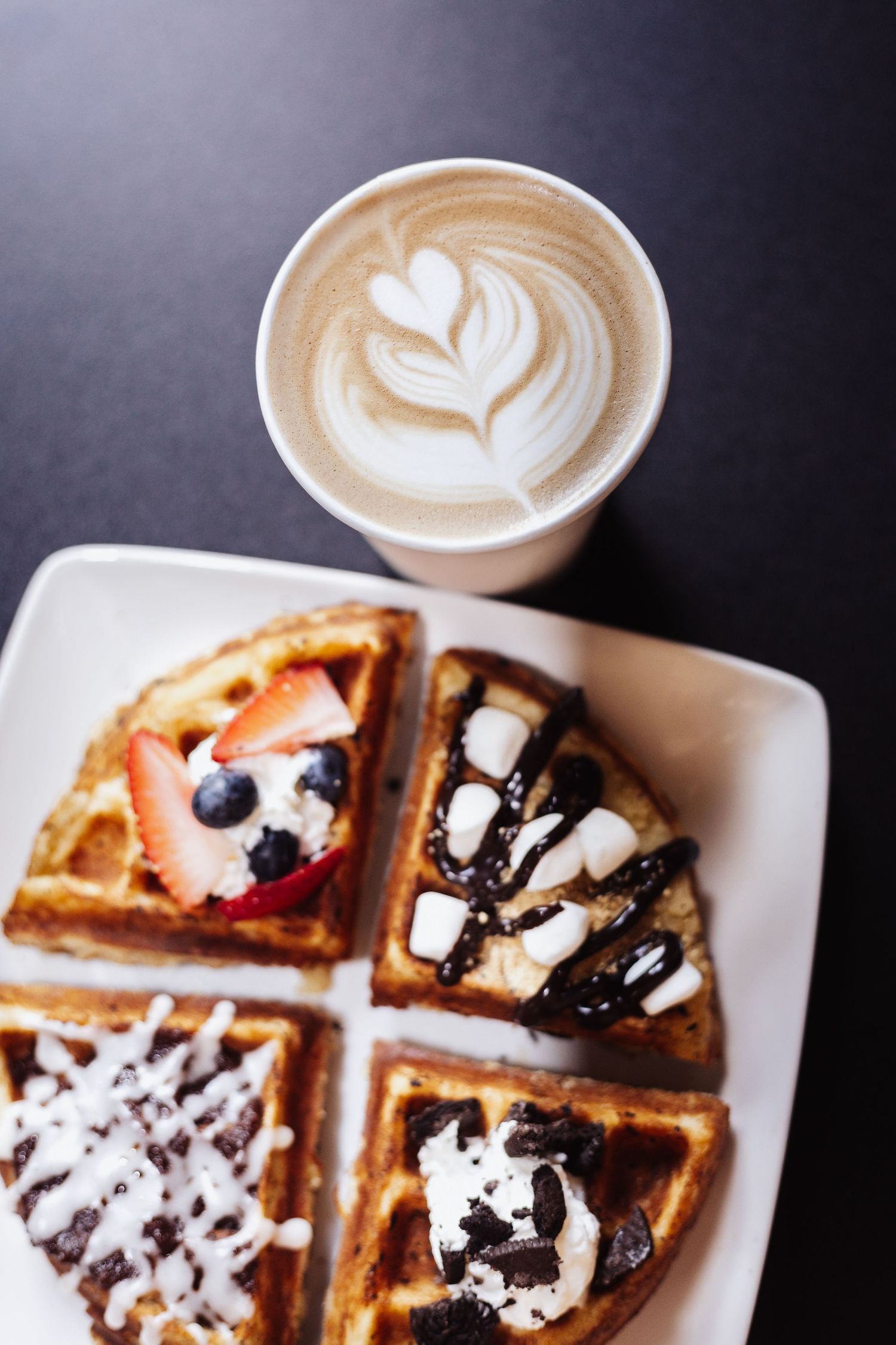 Belgian waffle topped with berries and cream next to latte art coffee.