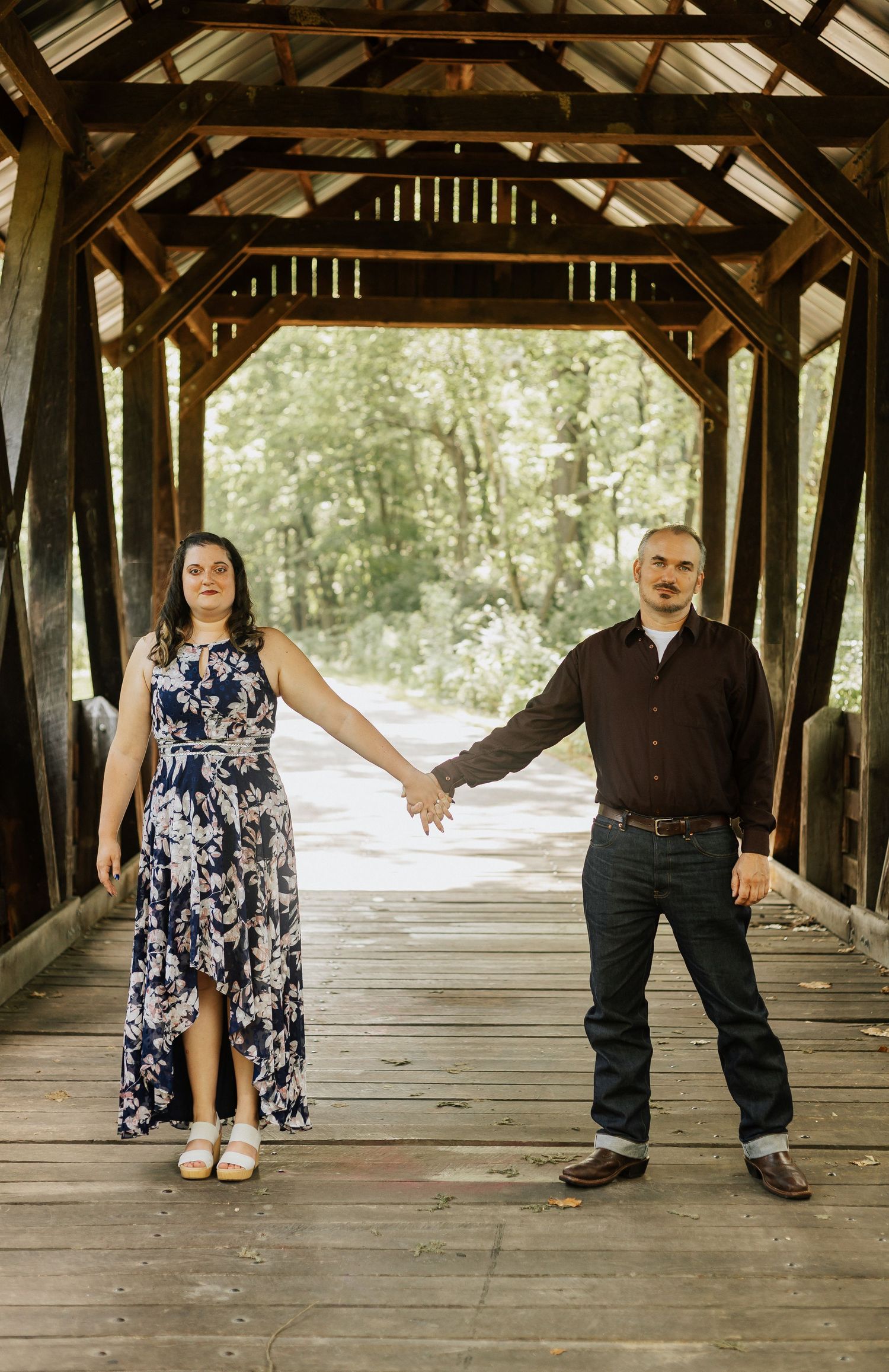 Couple poses creatively in a rustic covered bridge with wooden beams.