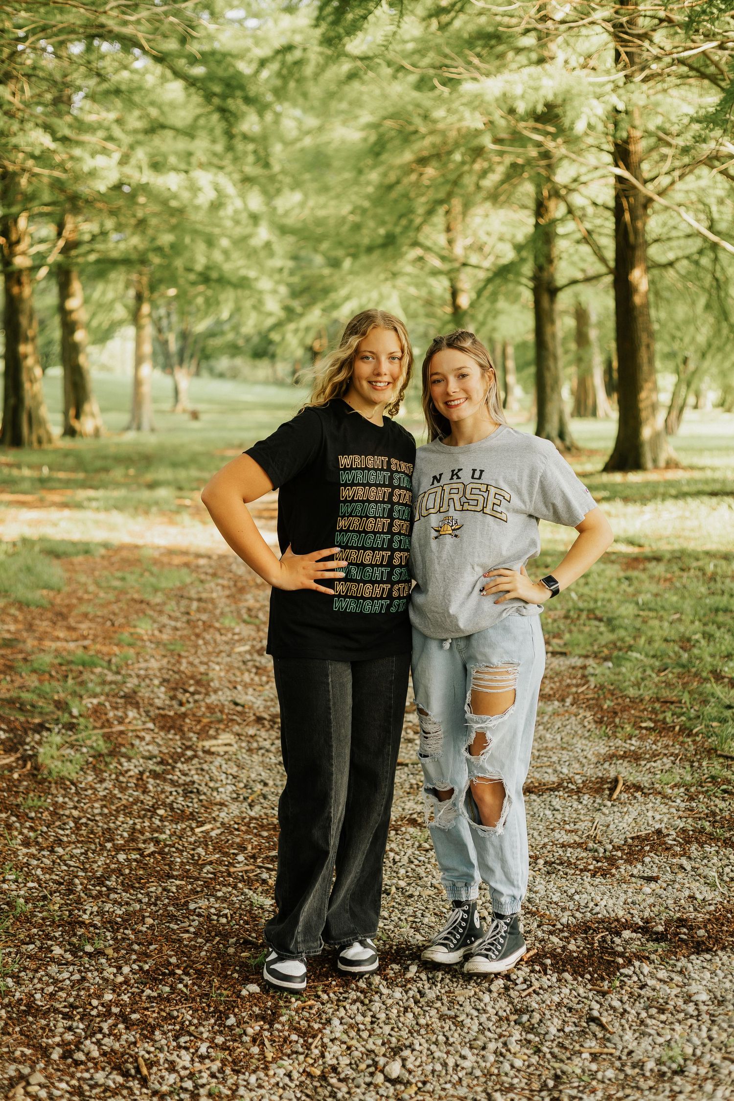Two friends in casual outfits posing together on autumn forest ground covered in leaves.