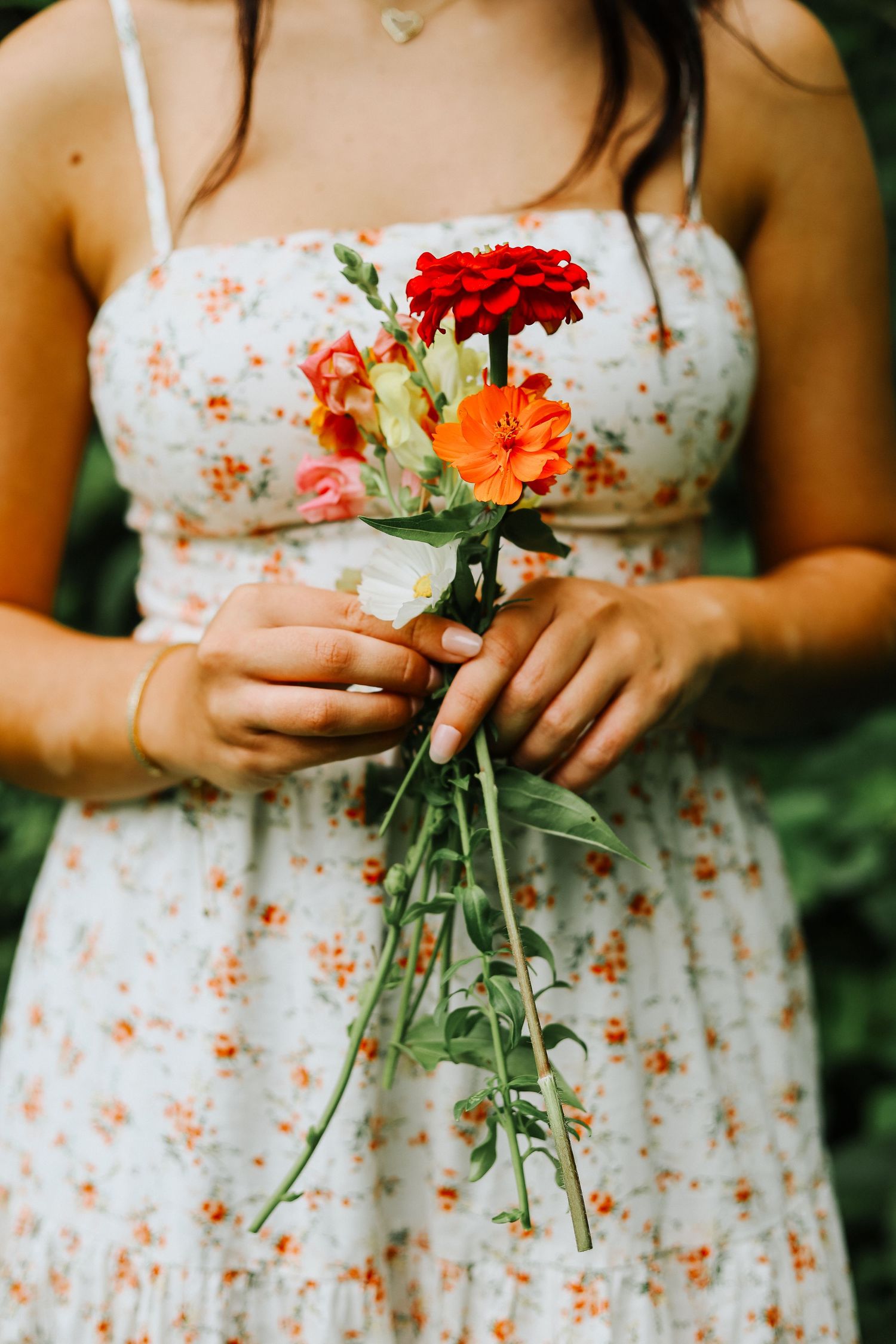 Close-up of hands holding freshly picked red and orange flowers in a floral dress.