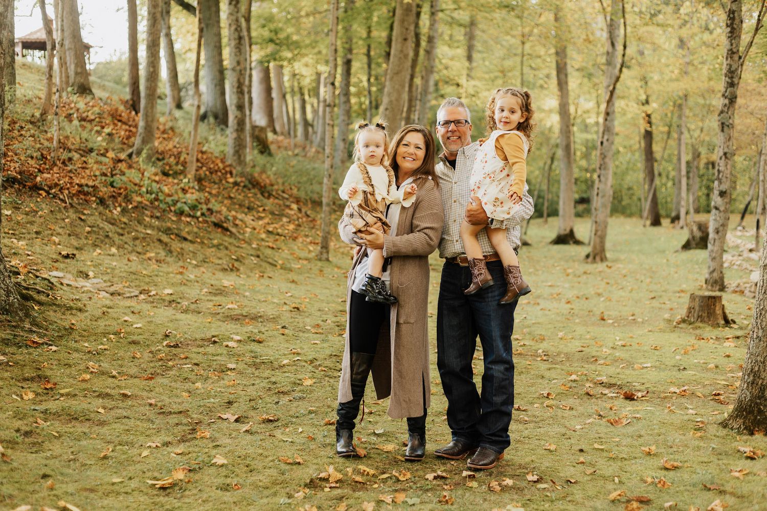 Outdoor family photoshoot in a wooded area with autumn trees.