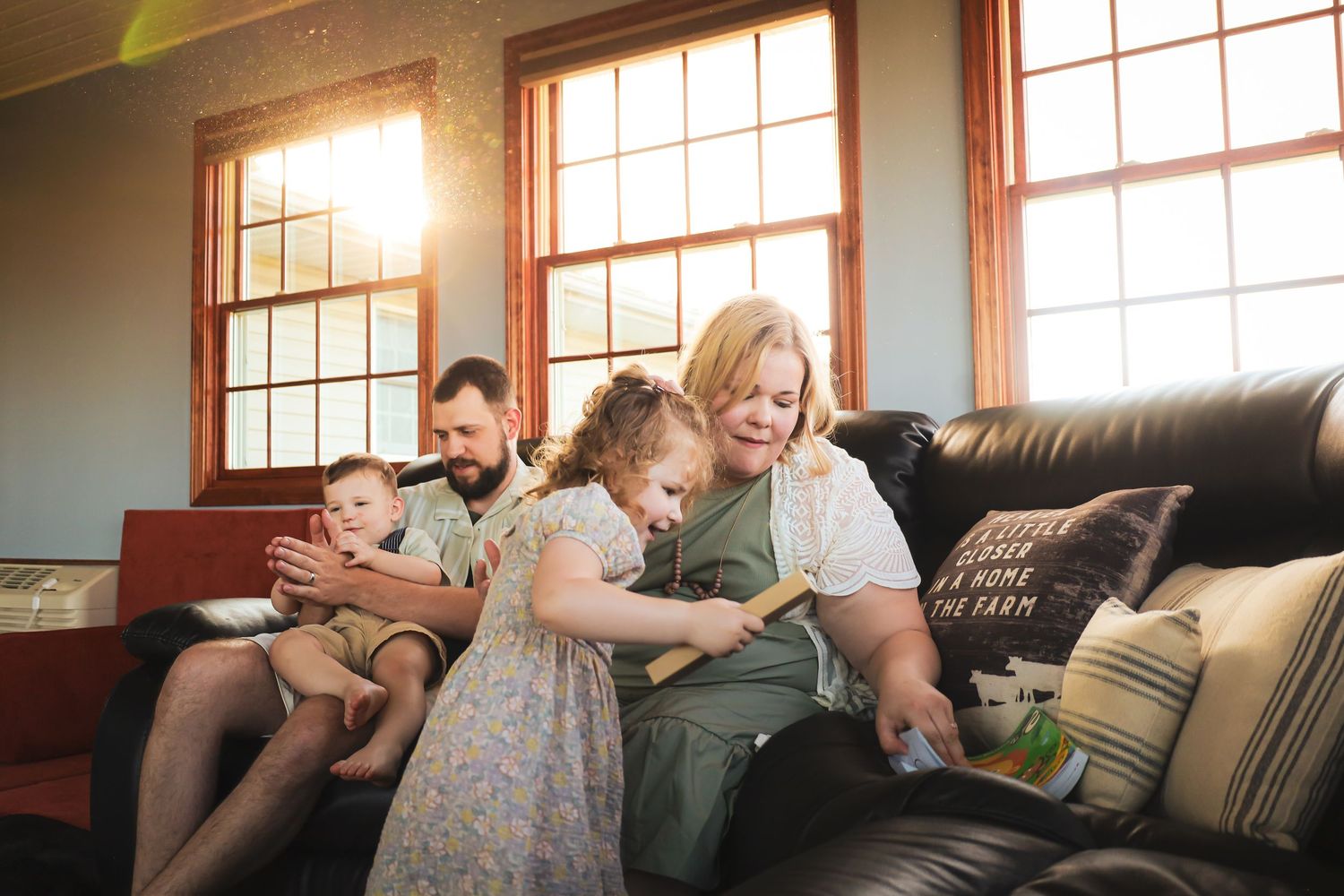 Family sharing tender moments together on a couch in a sunlit living room.