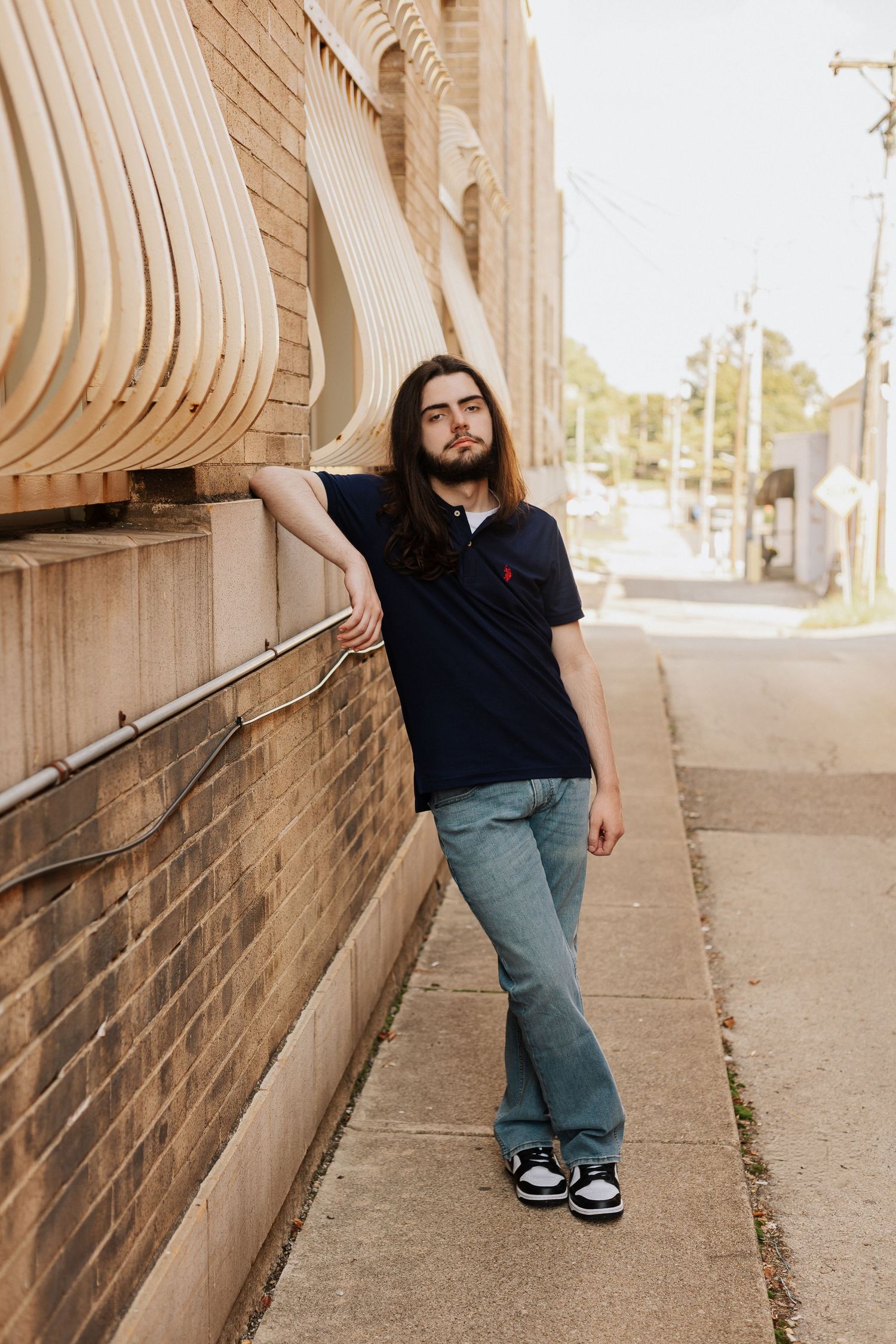 Person in navy polo and jeans leans against curved wooden wall on sidewalk.