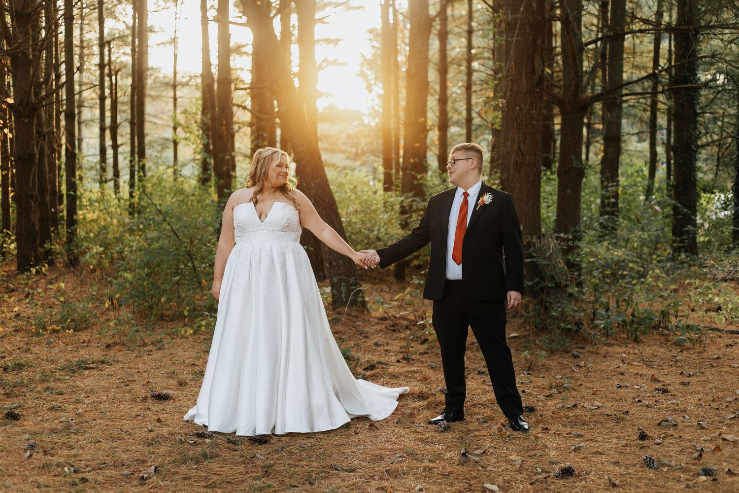 Wedding photography session in a pine forest with warm evening light streaming through trees.