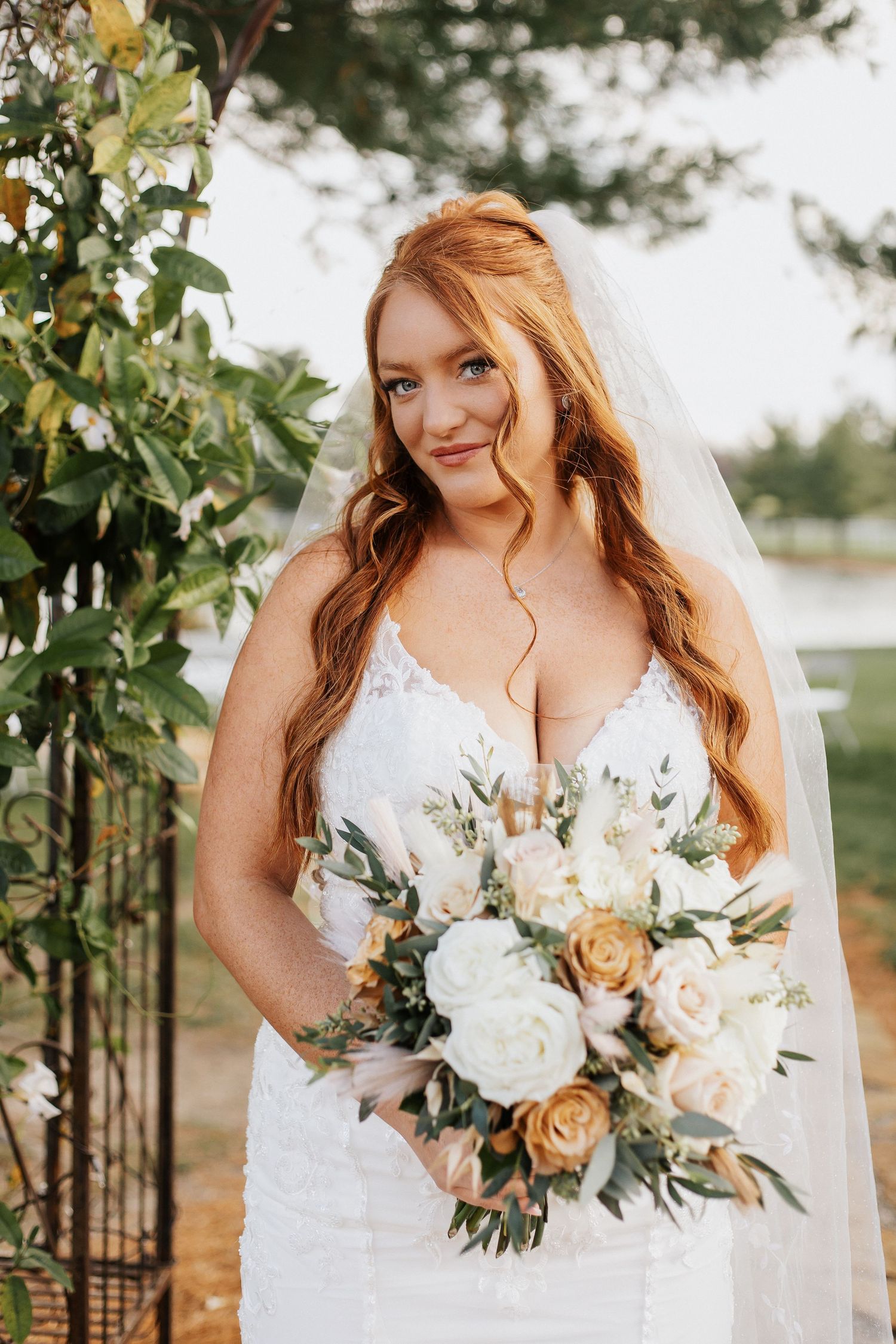 A wedding bouquet with white and peach roses paired with a lace white wedding dress in an outdoor garden setting.