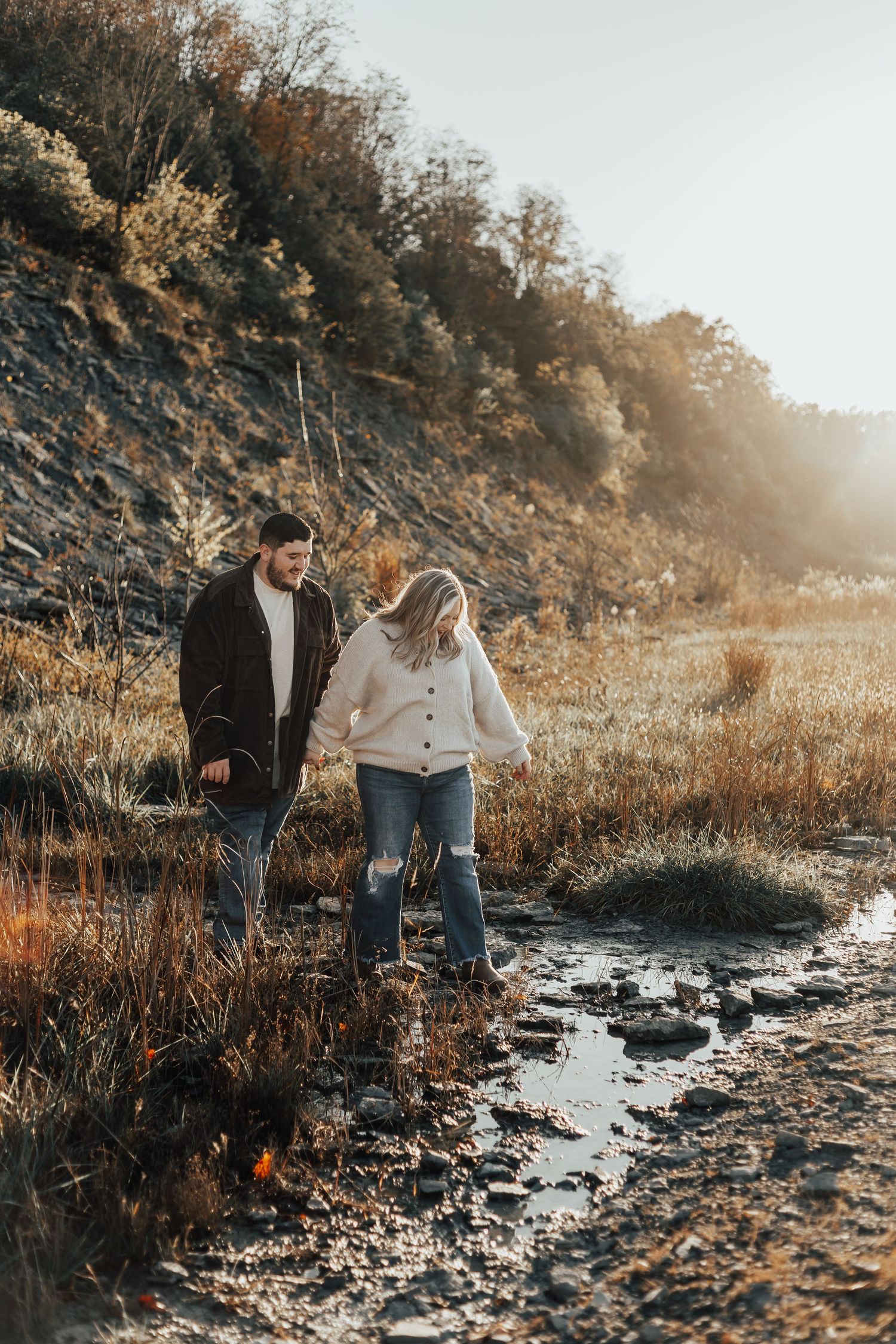 Couple walking along rocky trail with sunlit autumn scenery in background.