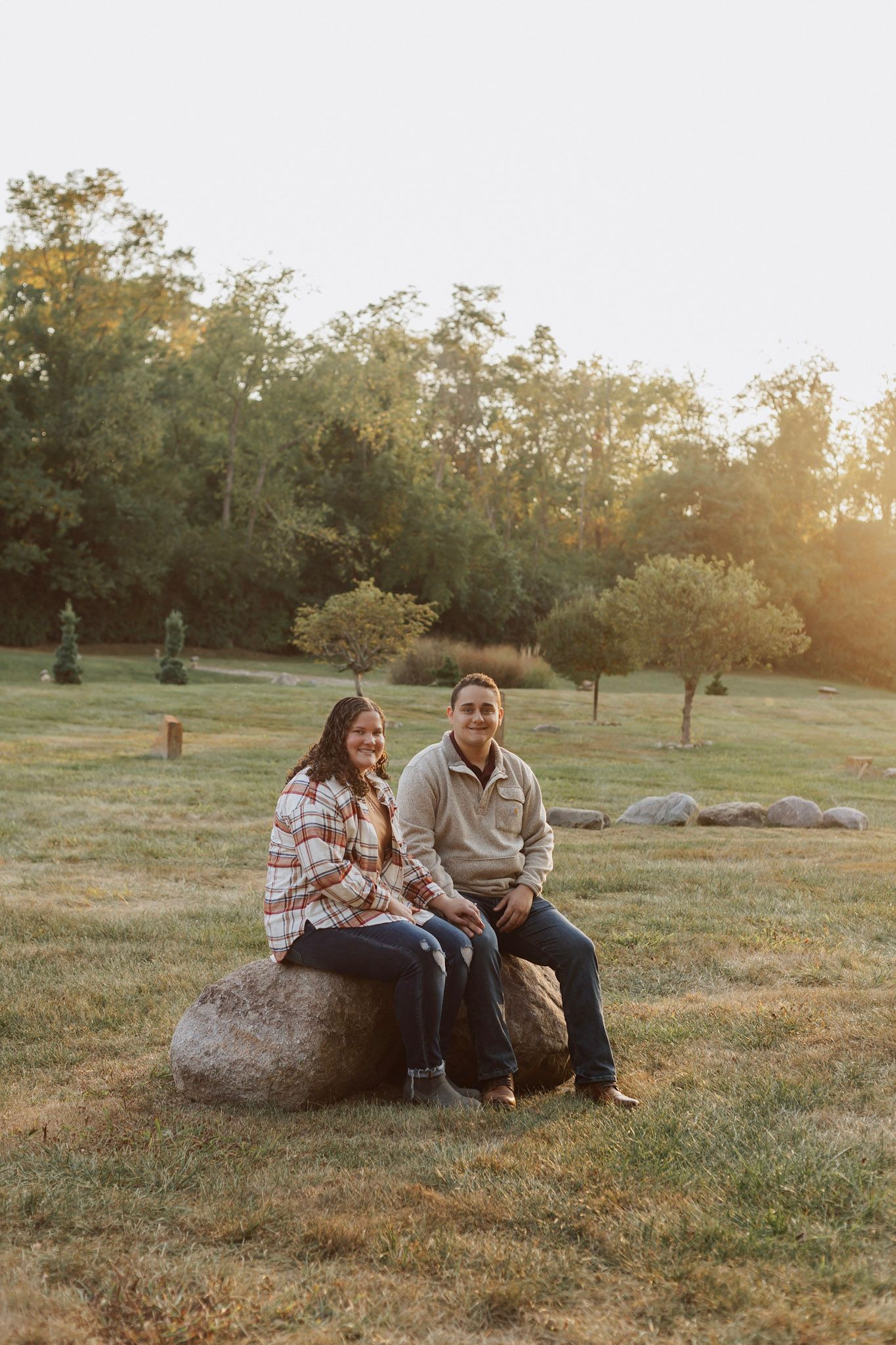 Couple sitting together on rocks at sunset in a grassy field.