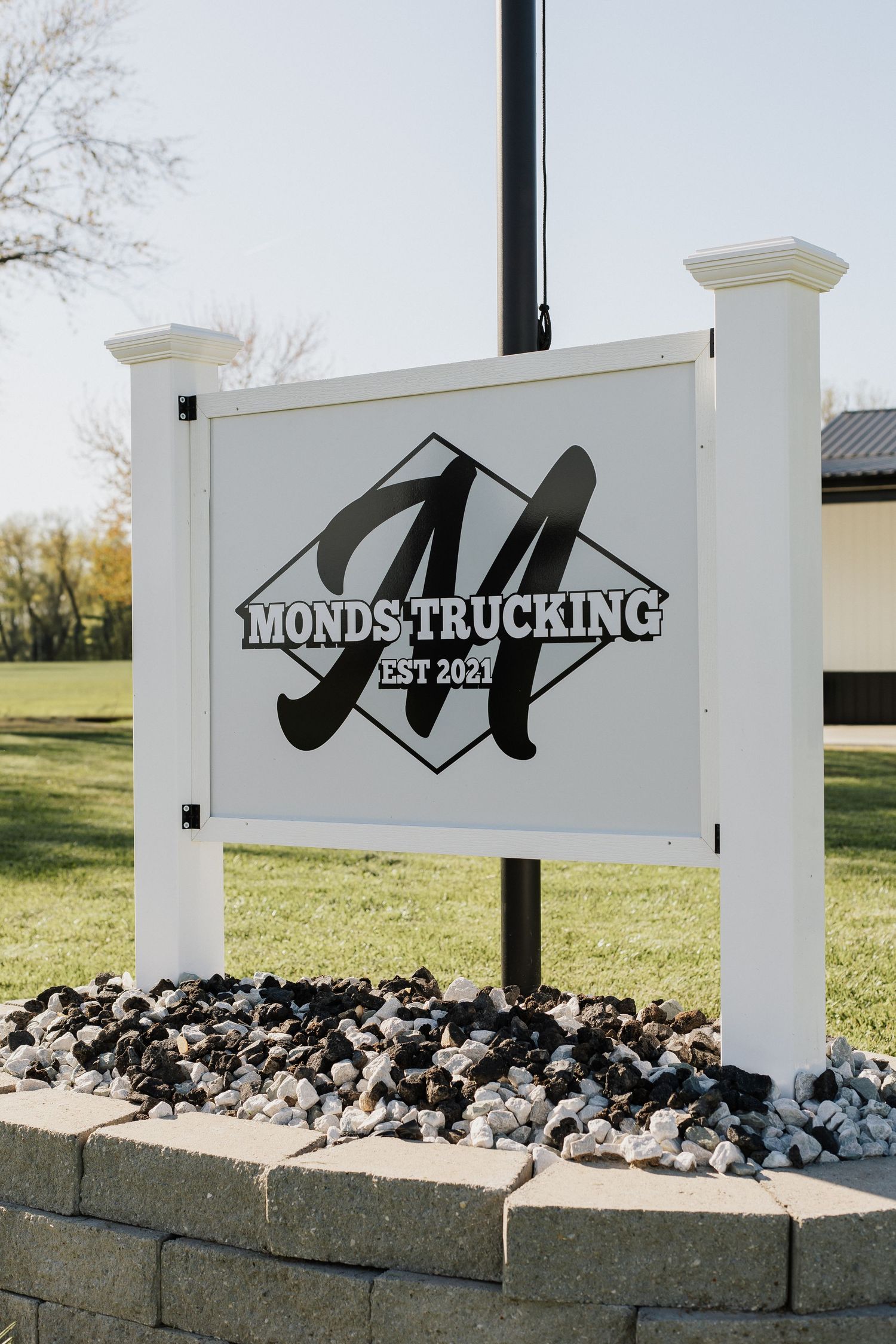 White stone entrance sign for Monds Trucking with decorative rock landscaping.
