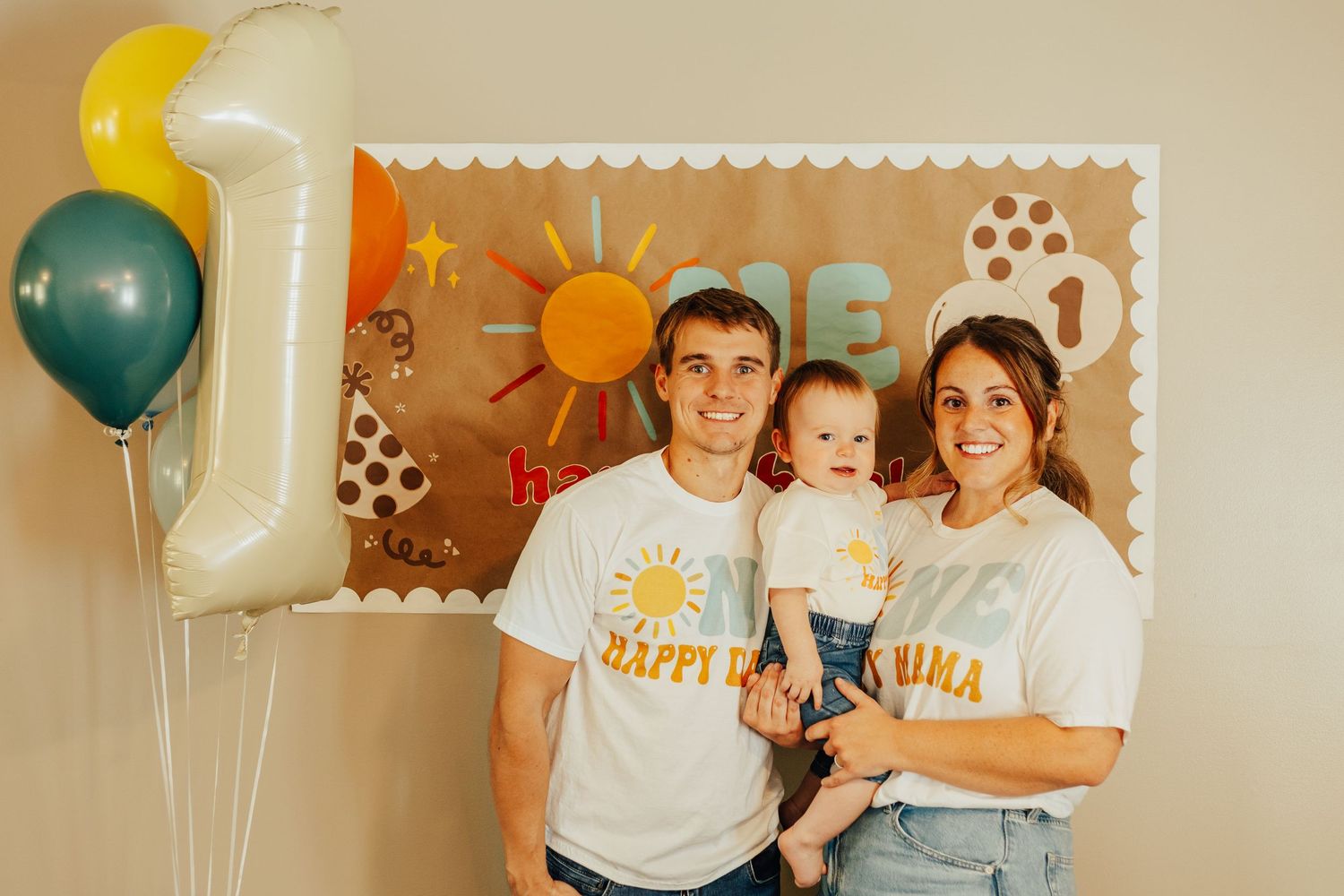 Family celebration with balloons and sun-themed backdrop featuring number one decoration.