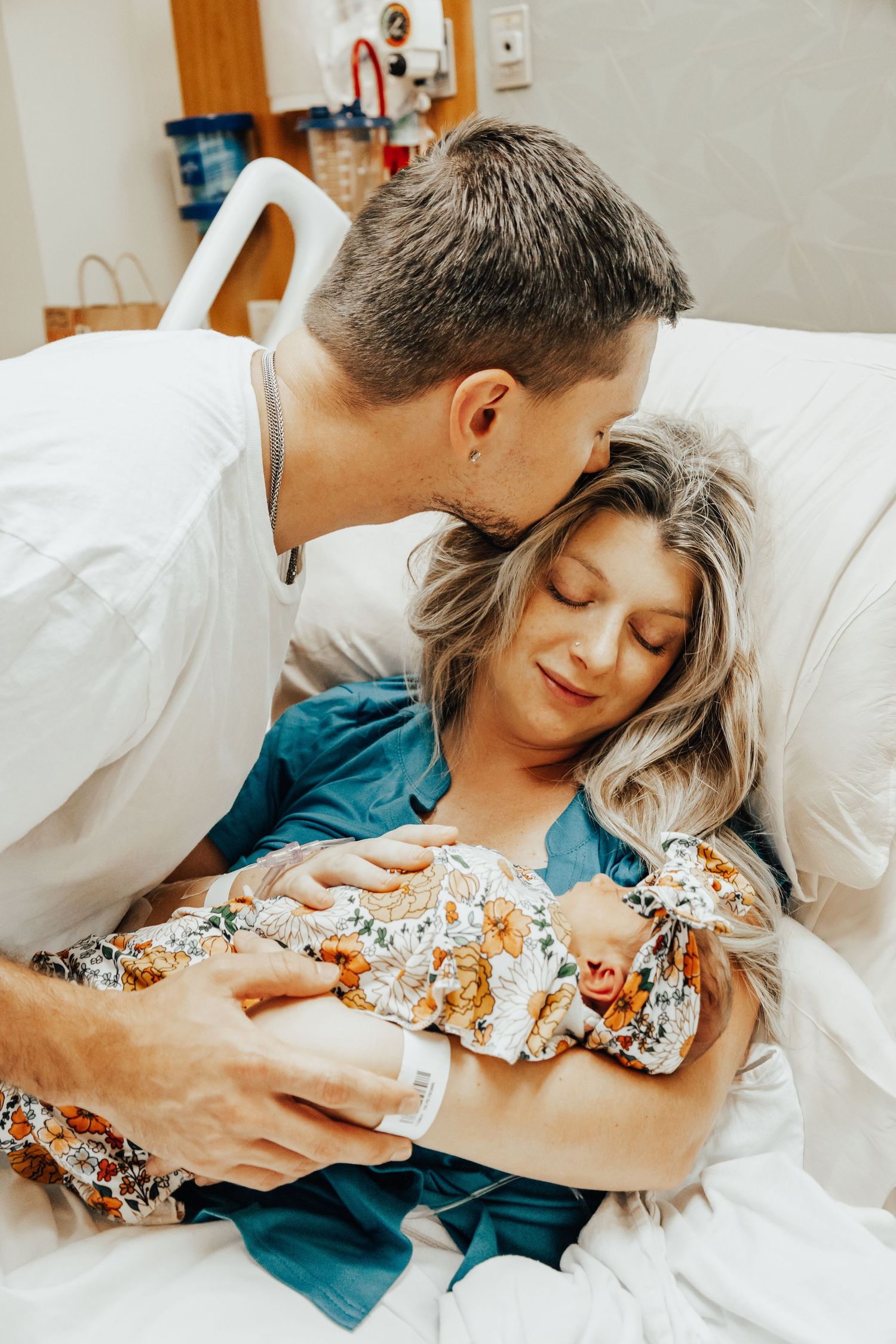 Parents lovingly cradling their newborn baby while resting on hospital bed.