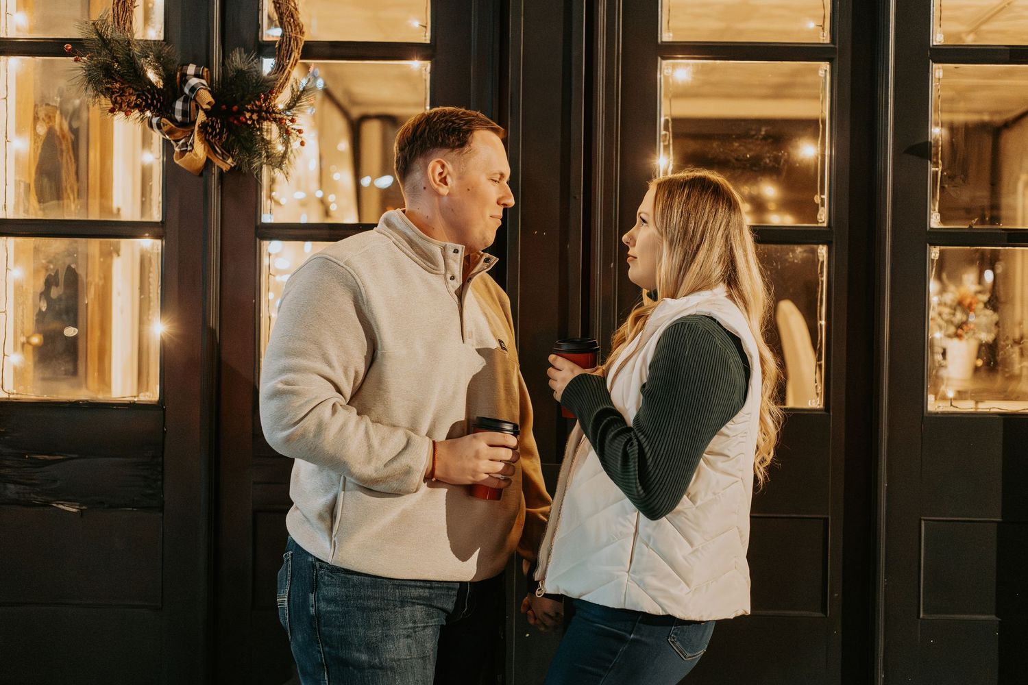 Couple enjoying drinks and conversation outside a warmly lit storefront.