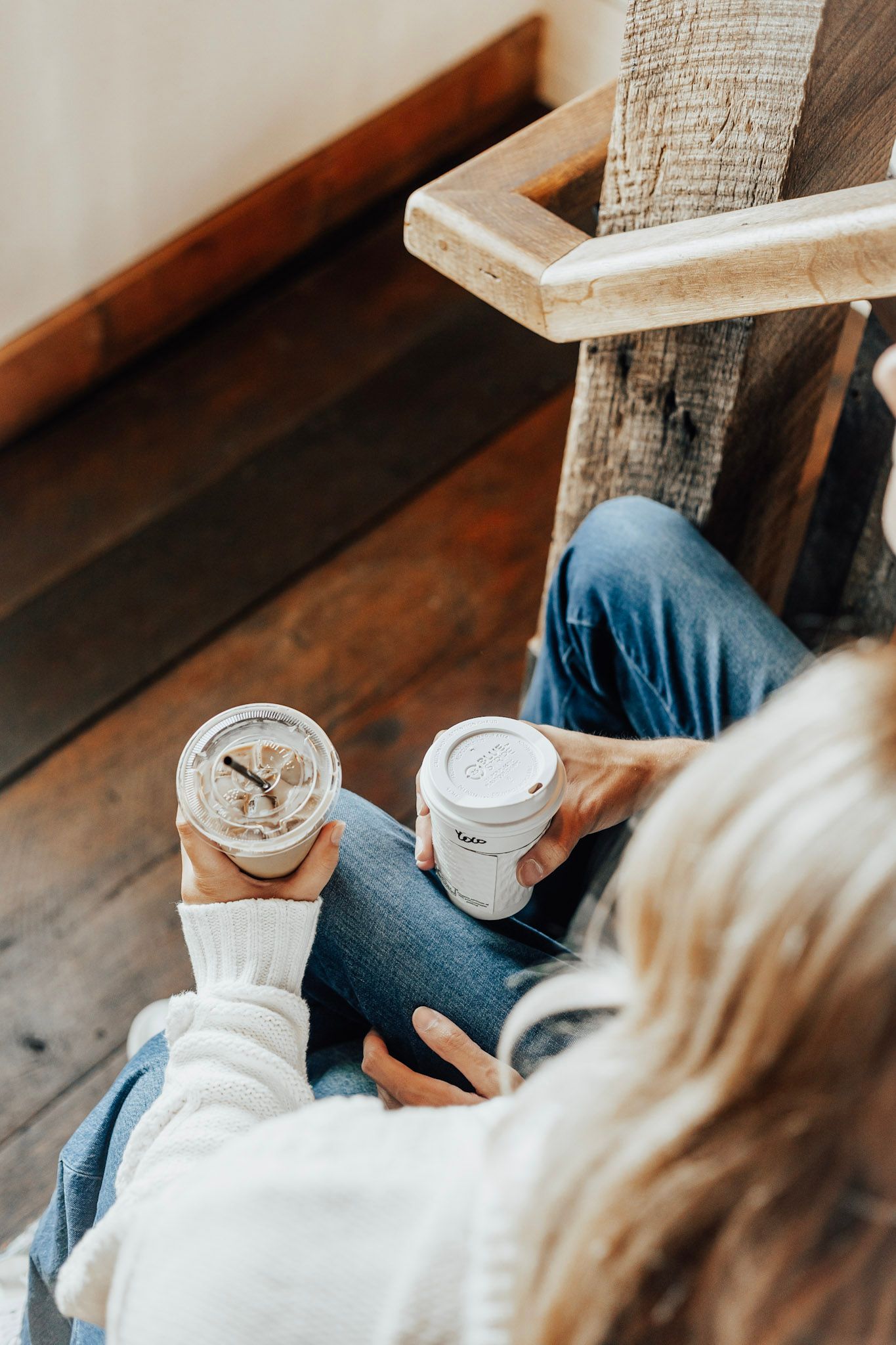 Close-up of hands holding coffee cups while sitting on wooden furniture.