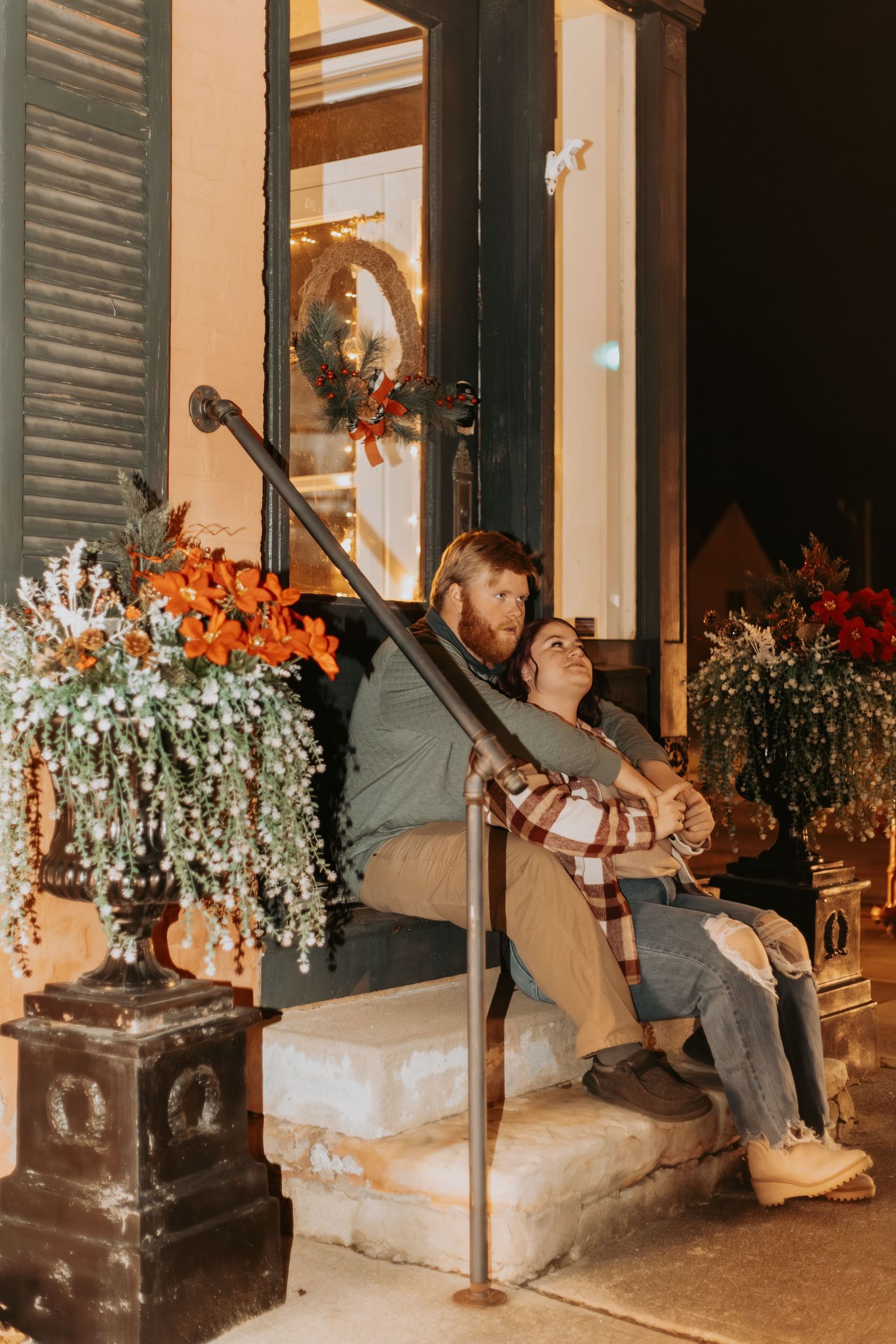 Couple sitting on outdoor steps with decorative floral arrangements and string lights creating a cozy atmosphere.