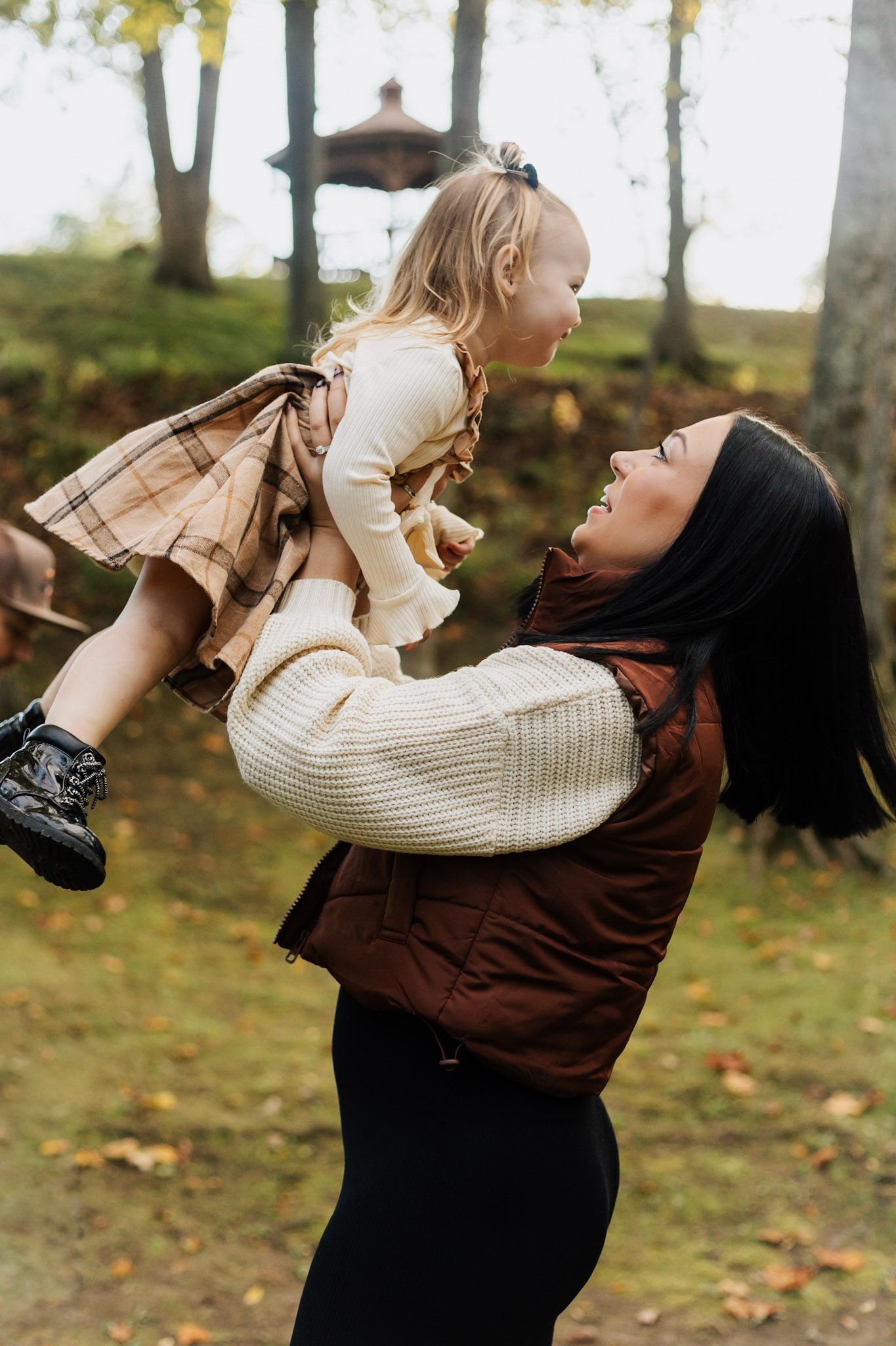 Playful moment captured outdoors with sweater and plaid clothing against autumn trees.