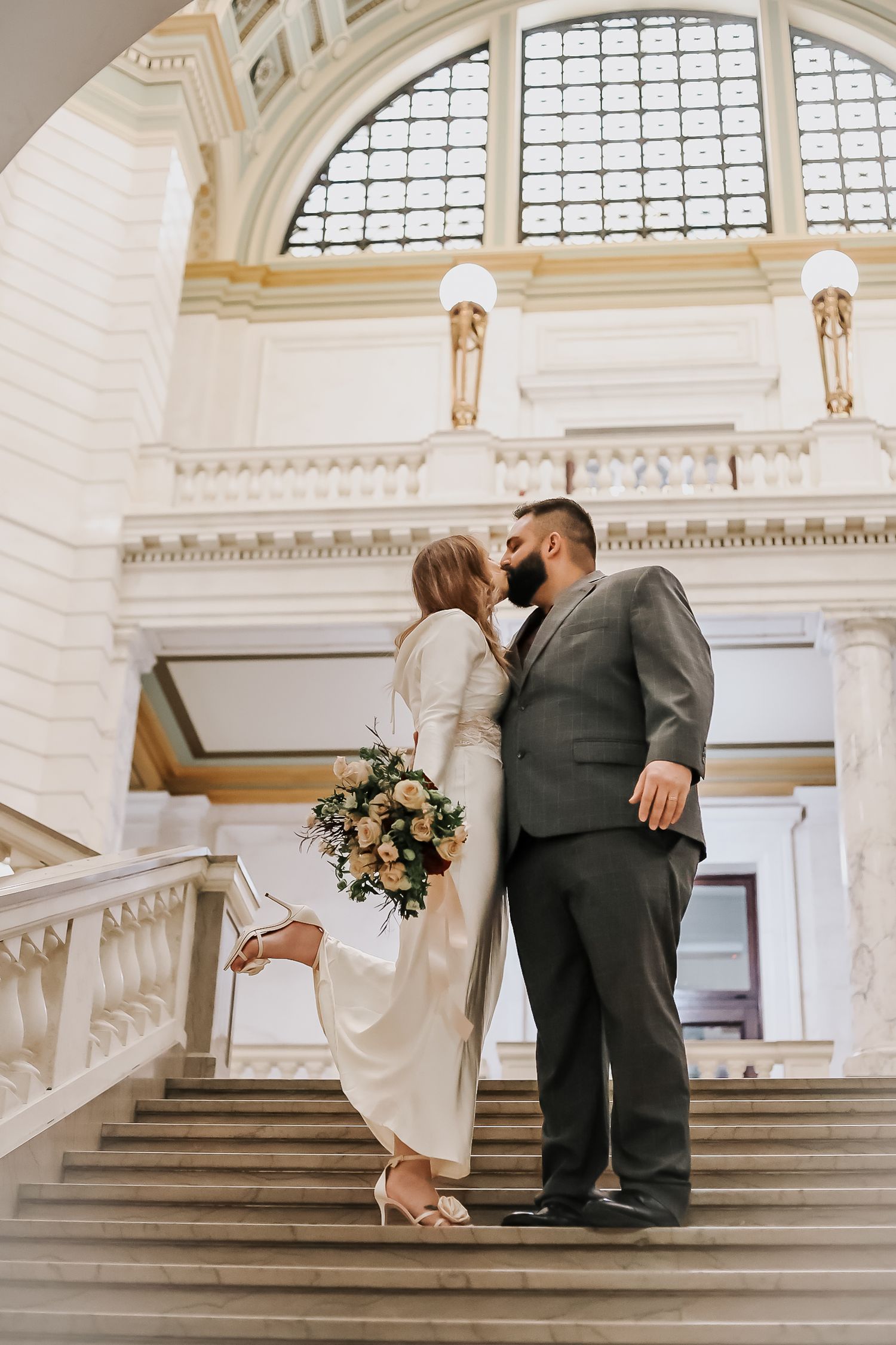 Romantic wedding photos on grand marble staircase with arched windows.