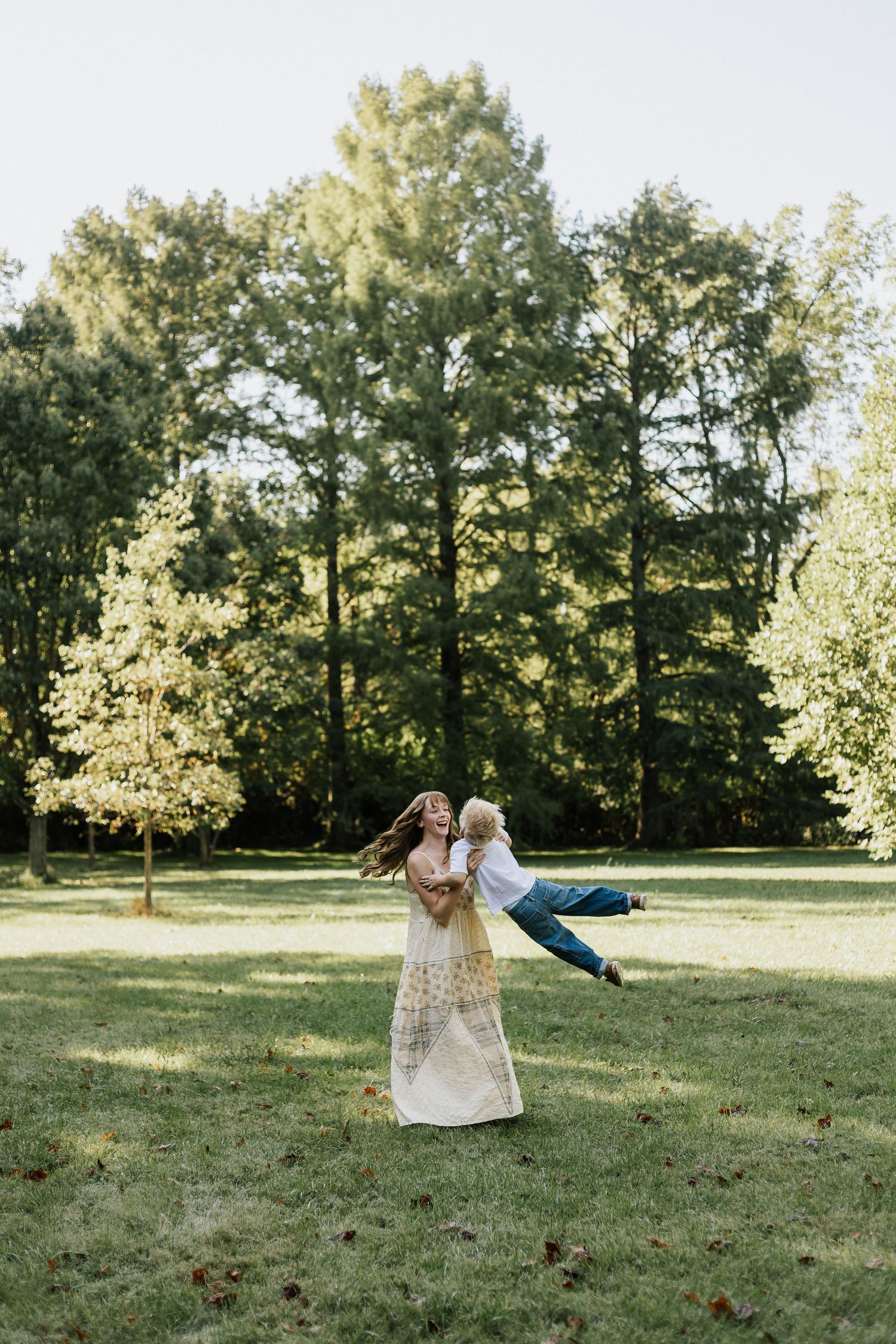 Joyful spinning moment captured in a sunlit park with tall trees in the background.