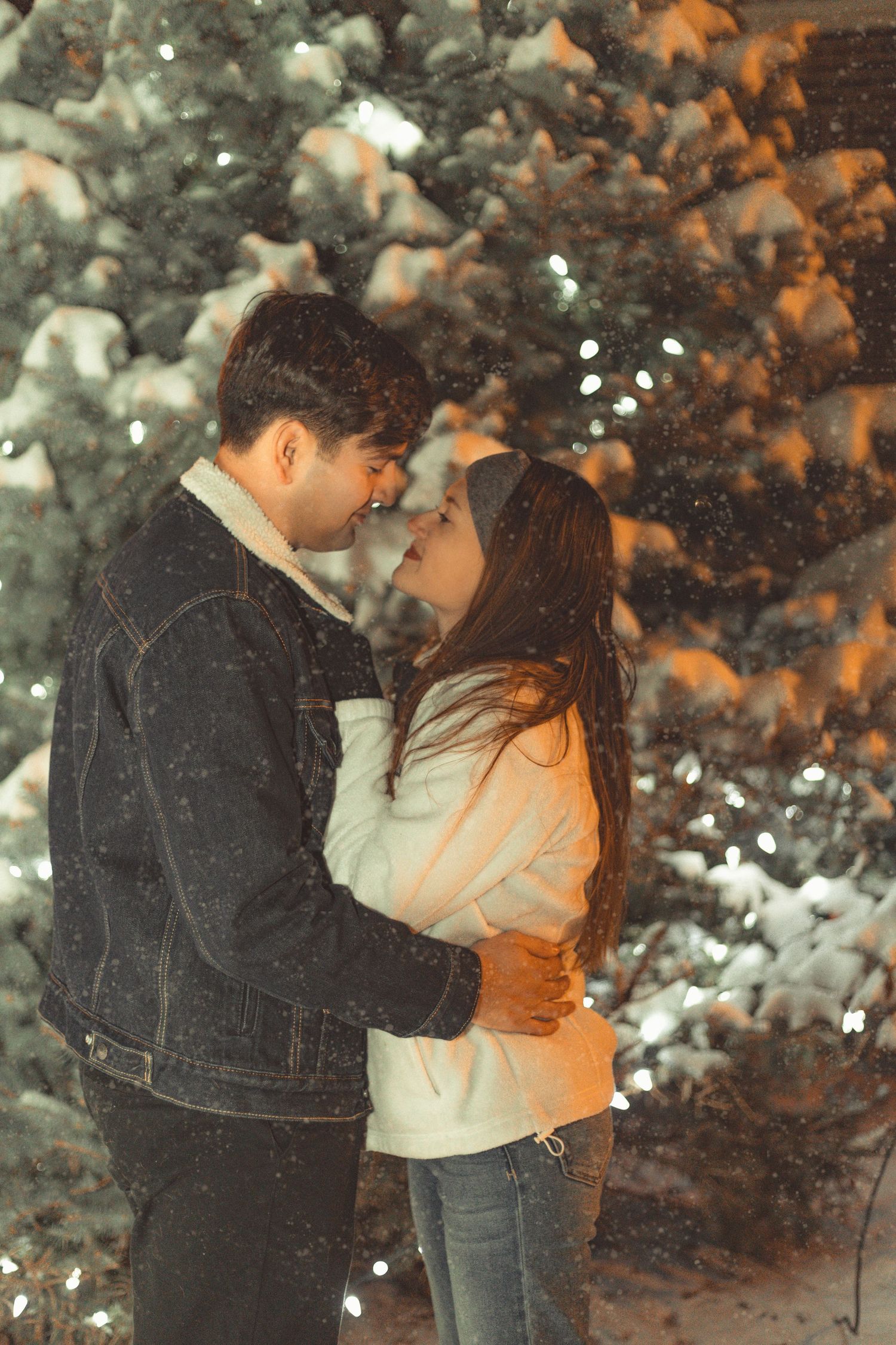 A romantic winter moment captured against snow-covered evergreen trees with falling snow.