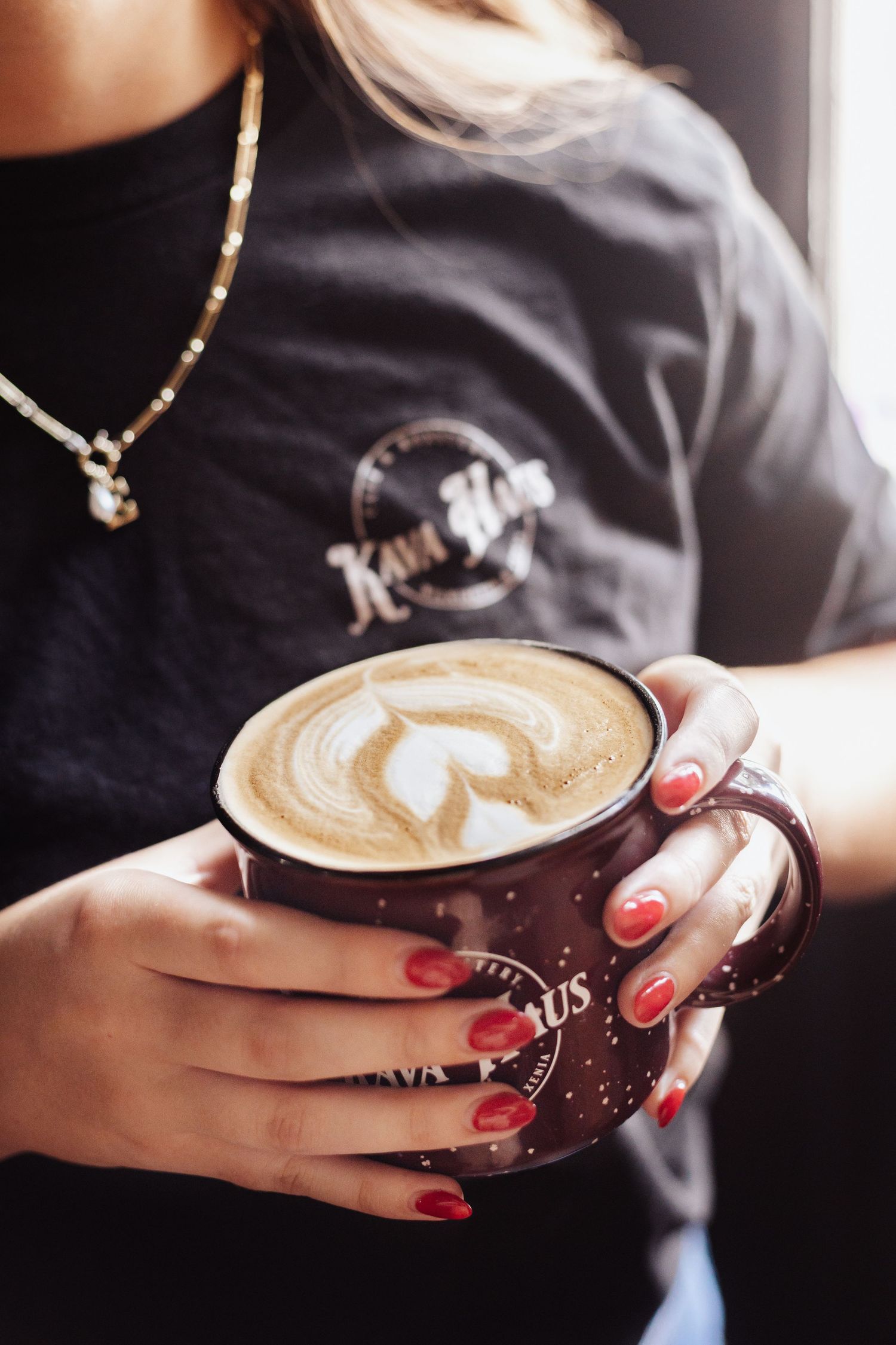 Hands holding latte with intricate heart-shaped foam art design.