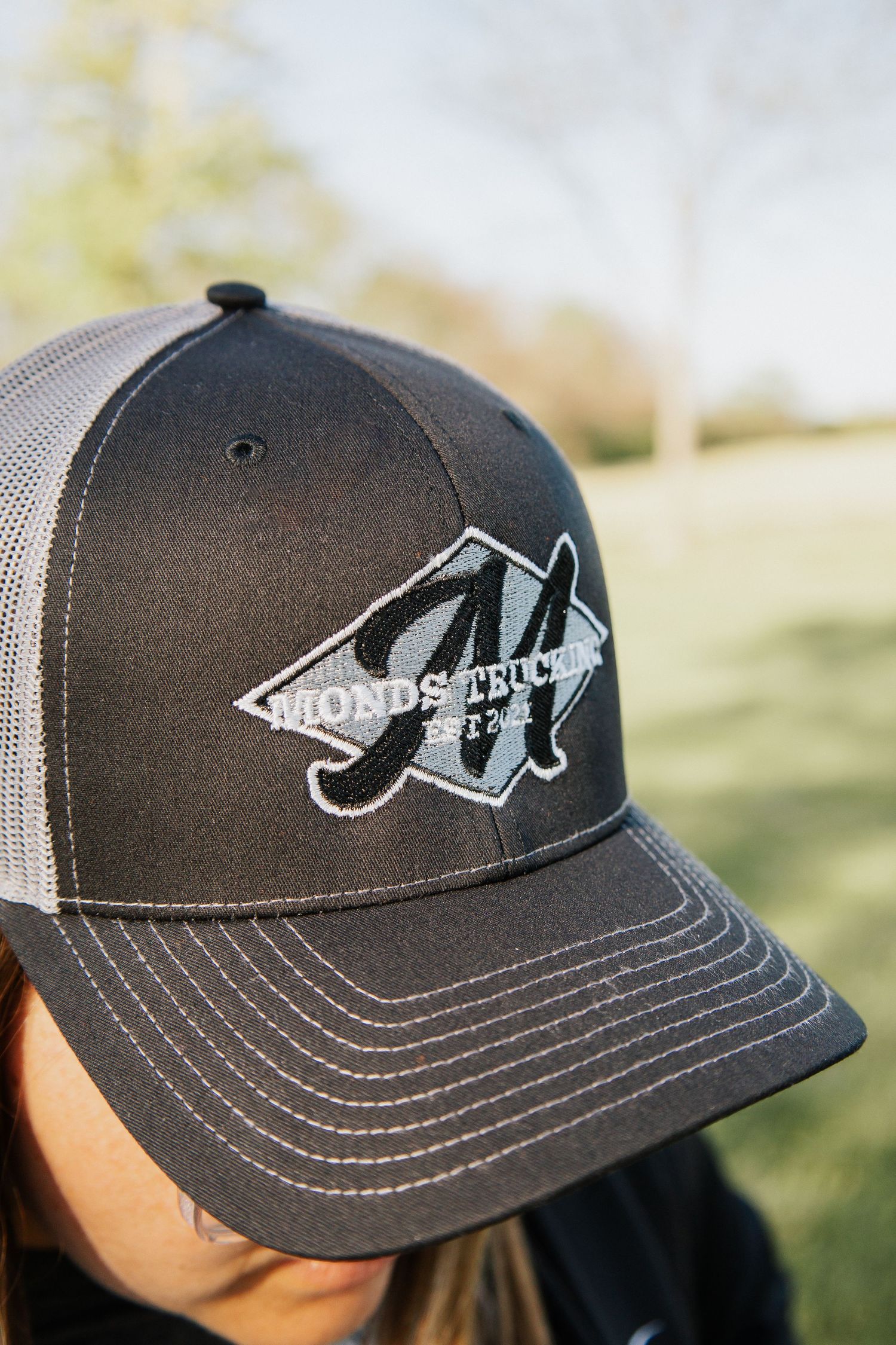 Black and gray trucker hat with embroidered company logo detail.