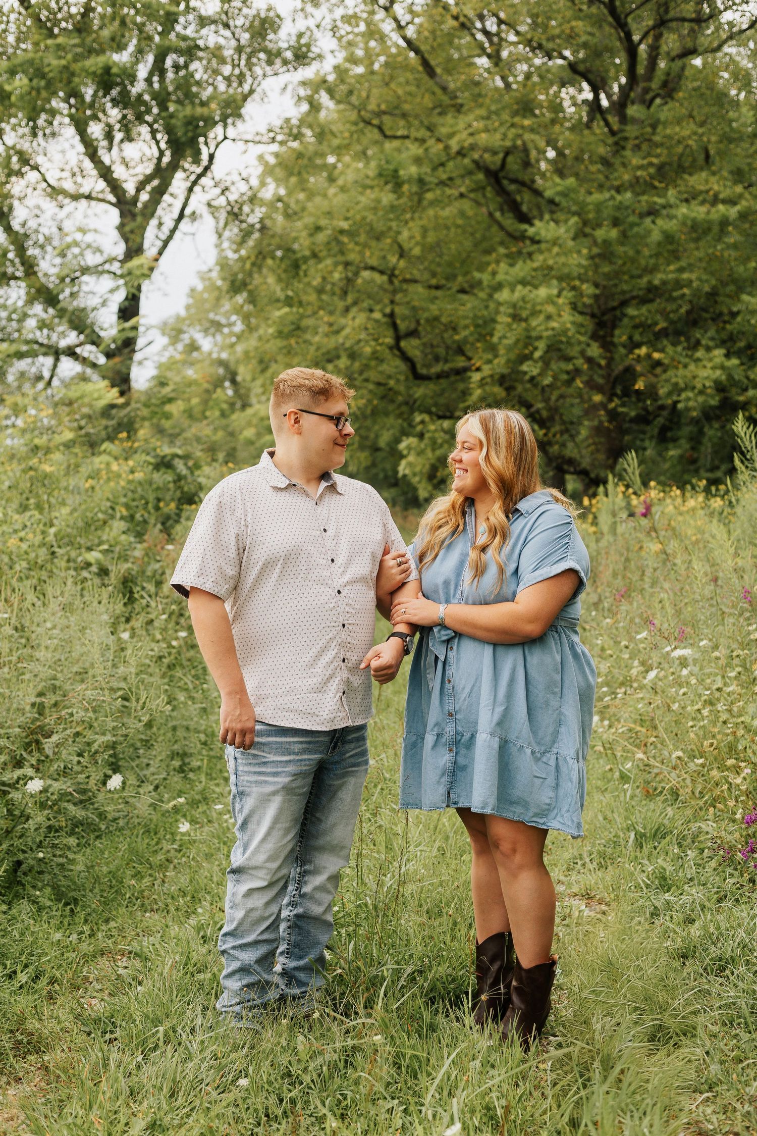Couple standing together in lush summer meadow with wildflowers and trees.