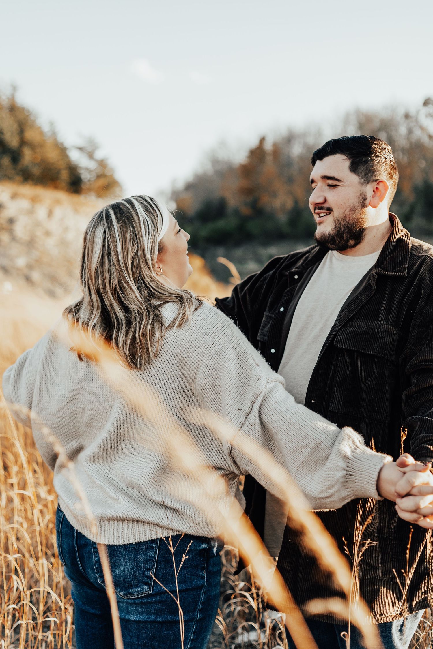 Couple sharing joyful moment in golden field during sunset photo session.