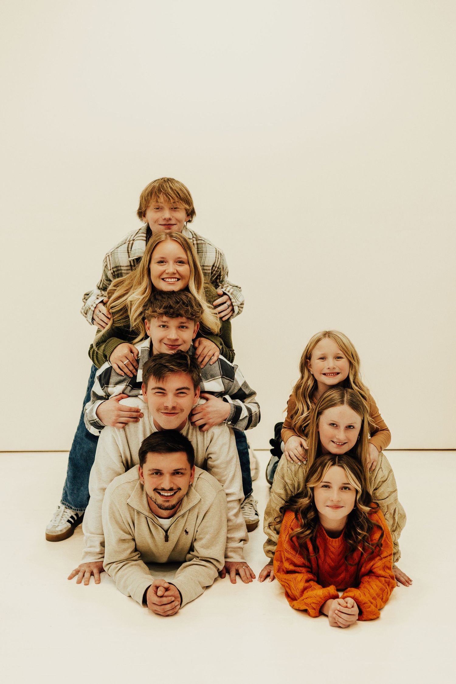 Family members stacked in playful pyramid pose against white background for portrait session.