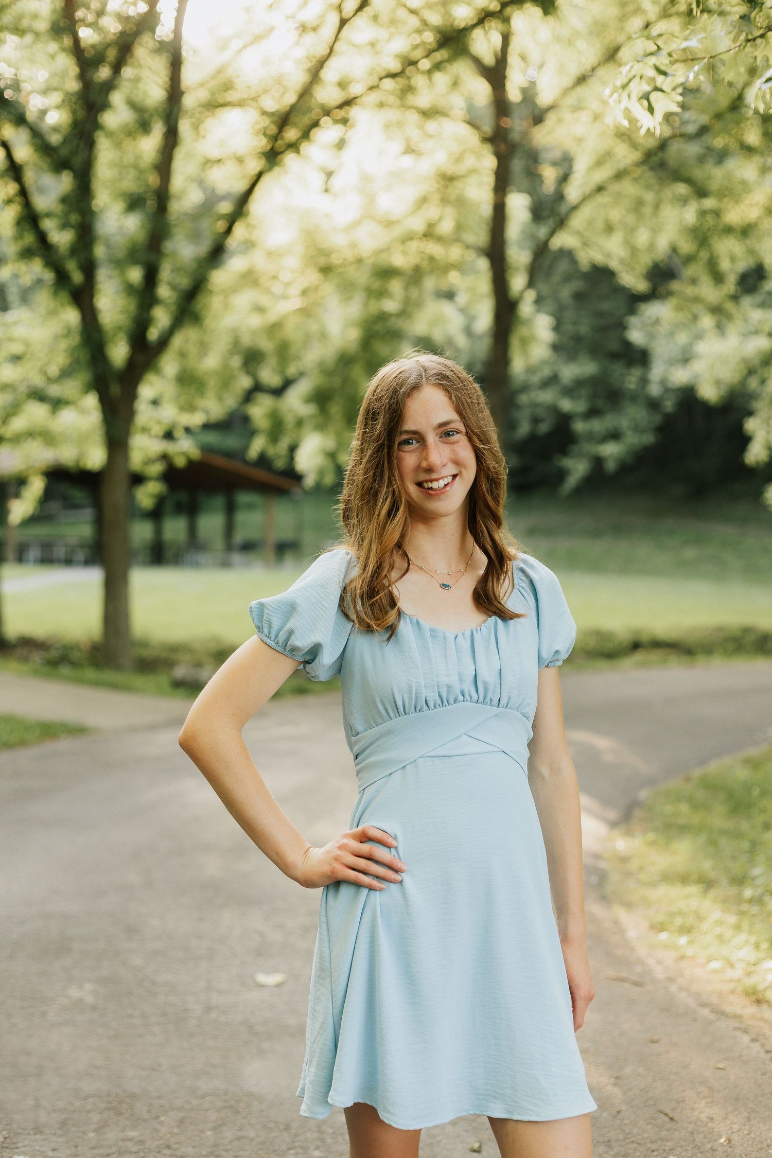 Summer portraits in a park wearing a light blue outfit against a backdrop of green trees.