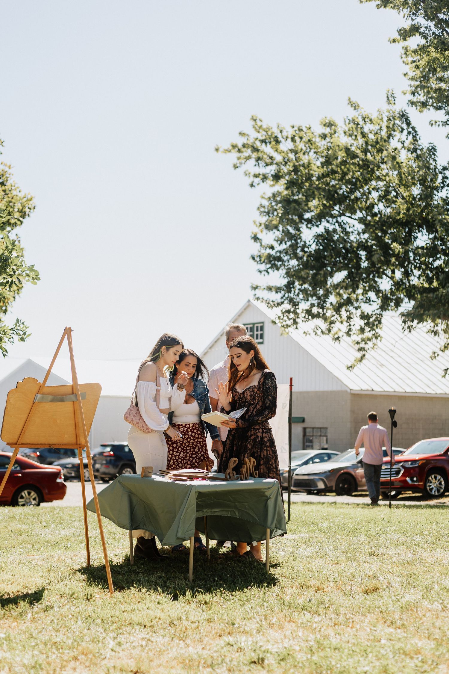 Outdoor wedding reception setup with seating areas on a grassy field under summer skies.