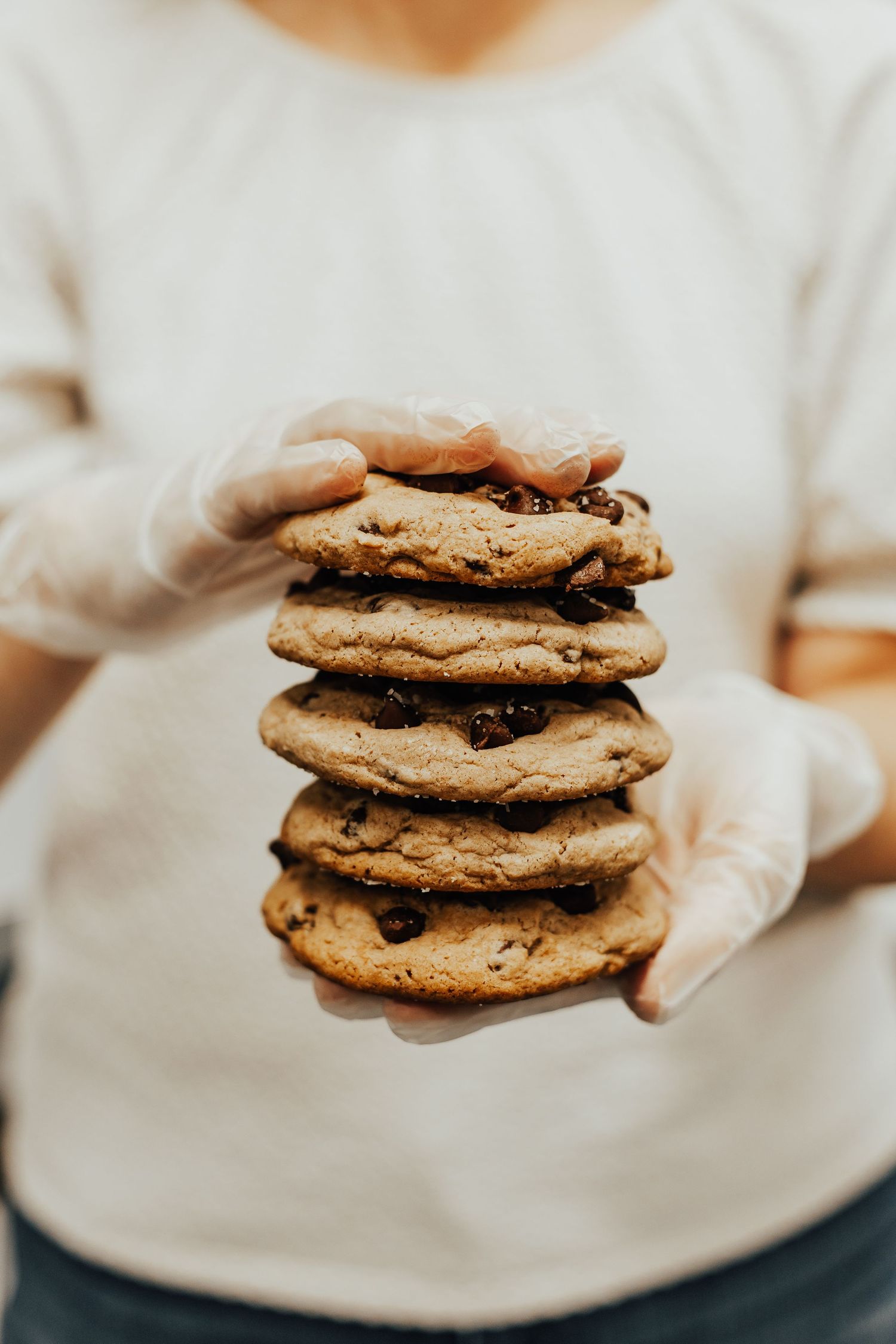 Stack of fresh chocolate chip cookies being held with white gloves.
