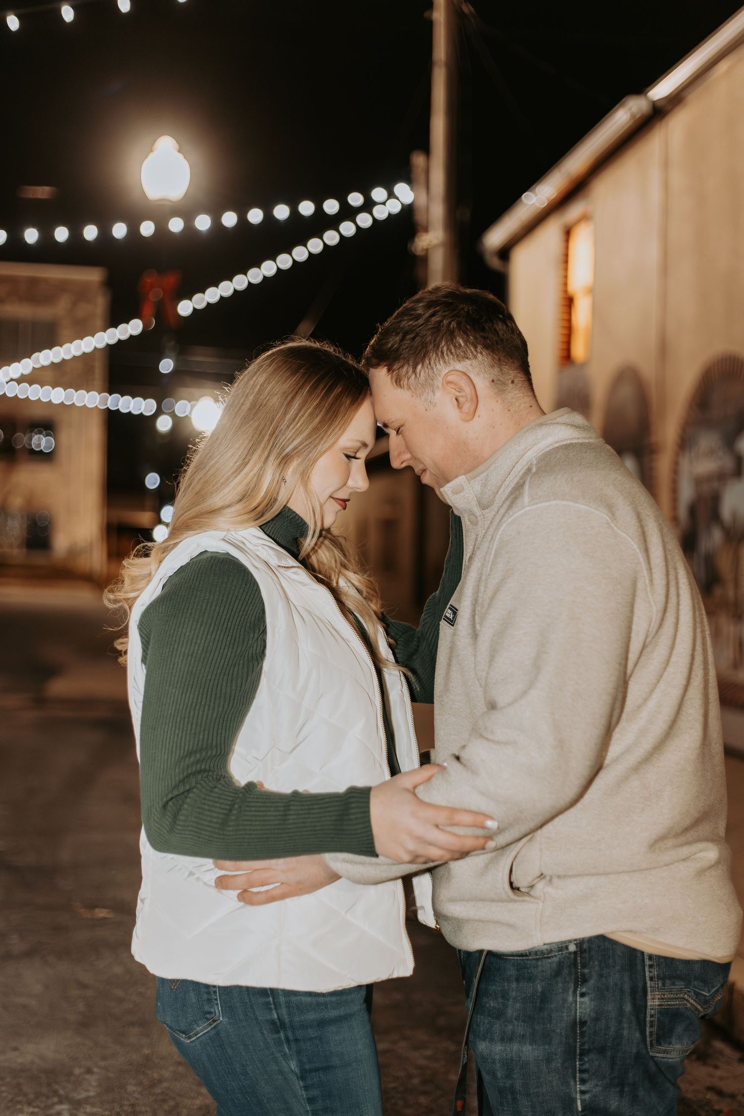 Intimate moment shared between couple beneath decorative outdoor lighting.
