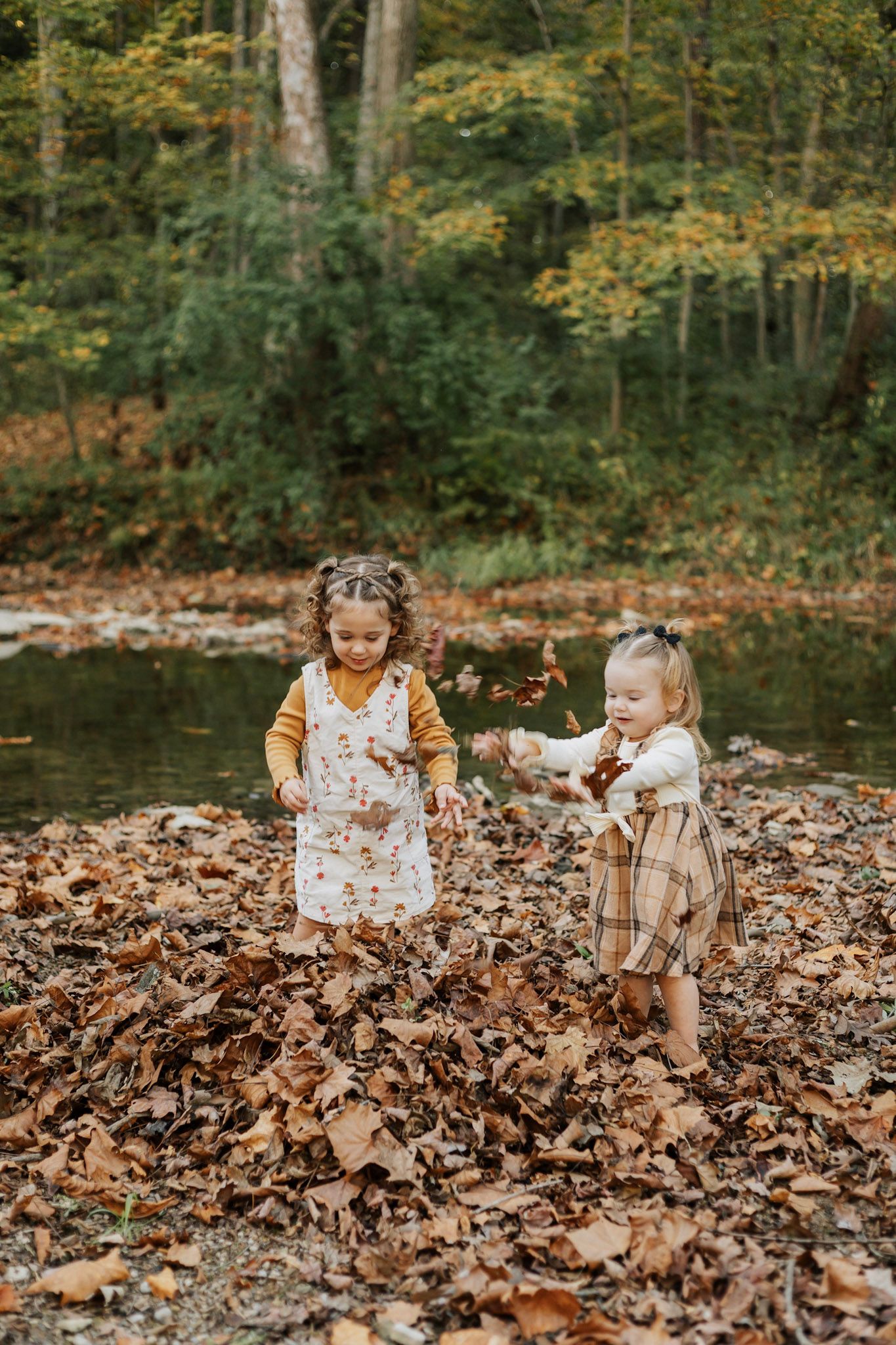 Children playing in fallen autumn leaves by a creek in the woods.
