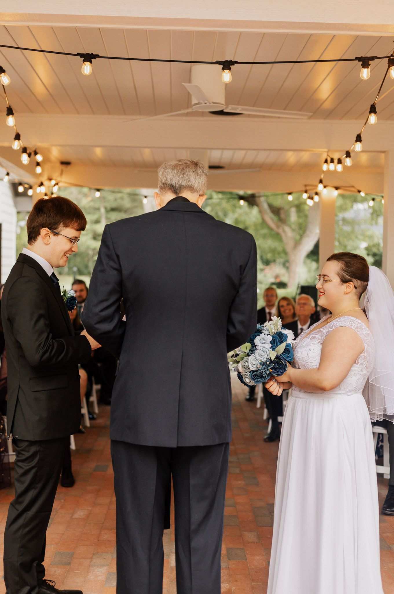 Wedding ceremony taking place under a covered pavilion decorated with string lights.