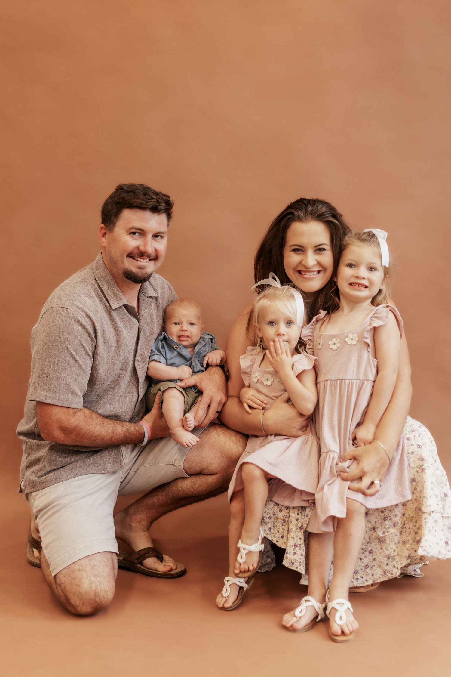 Family portrait with parents and three children against terracotta colored background.