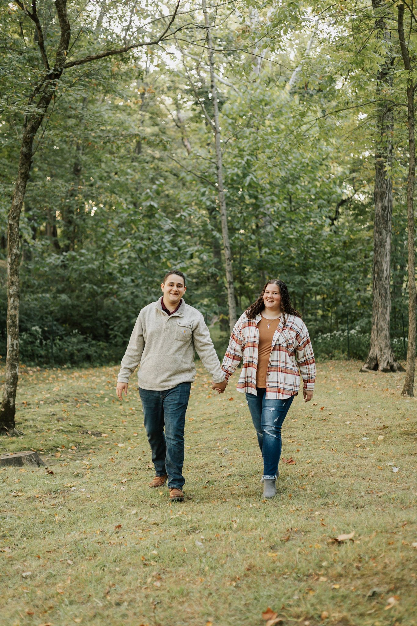 Couple walking together through a green wooded area in casual attire.
