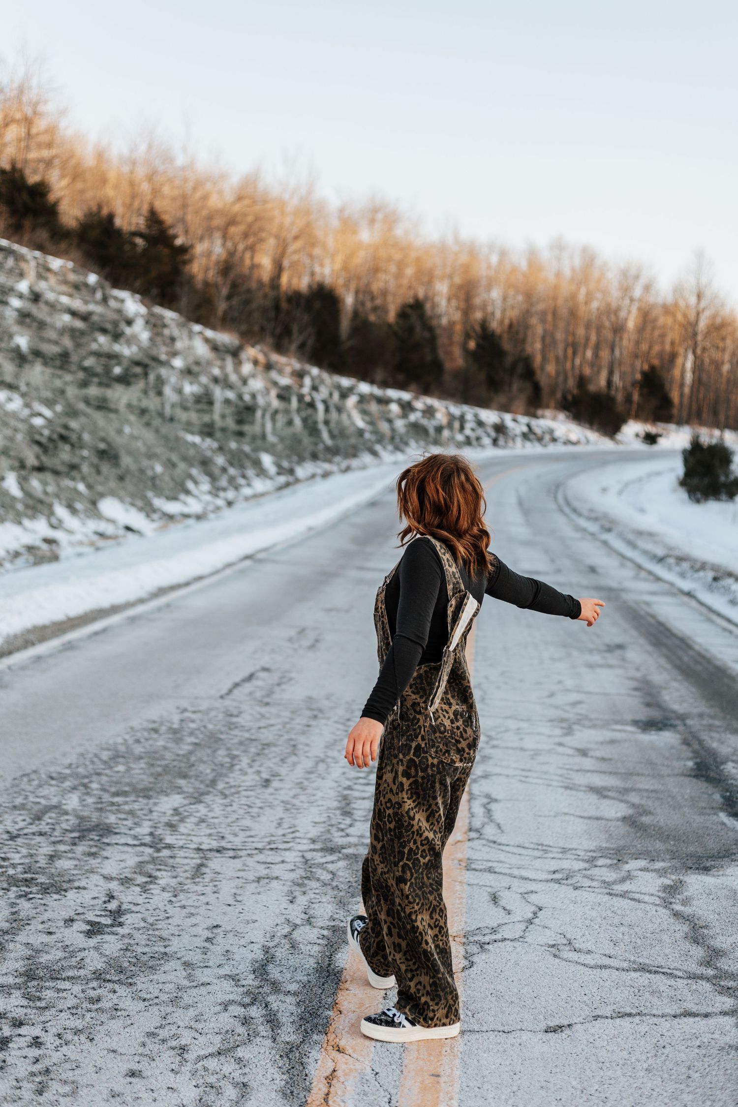 Person in a sparkly dress dances and twirls on a snowy winter road at sunset.