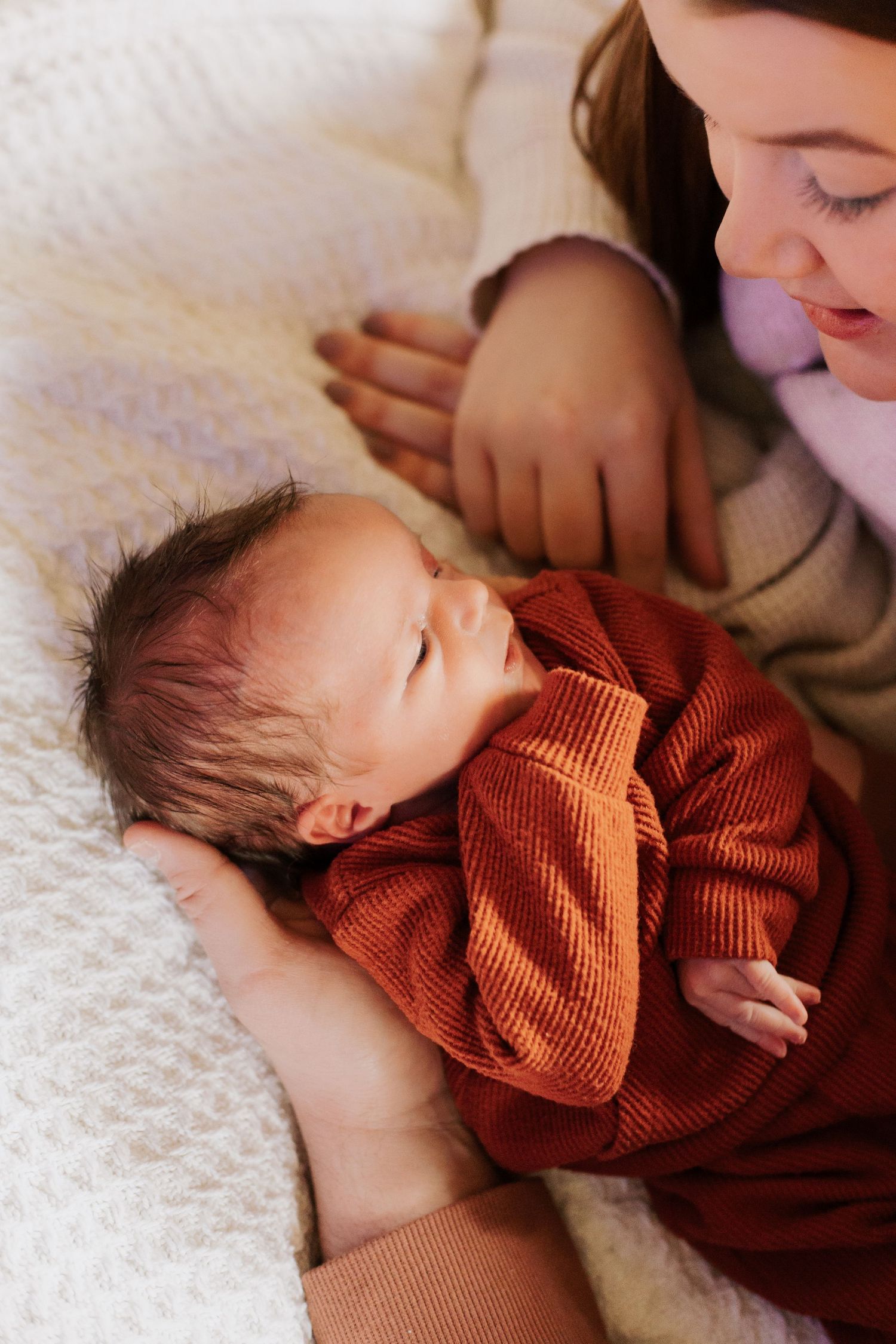 Peaceful newborn in orange sweater resting on white textured blanket.