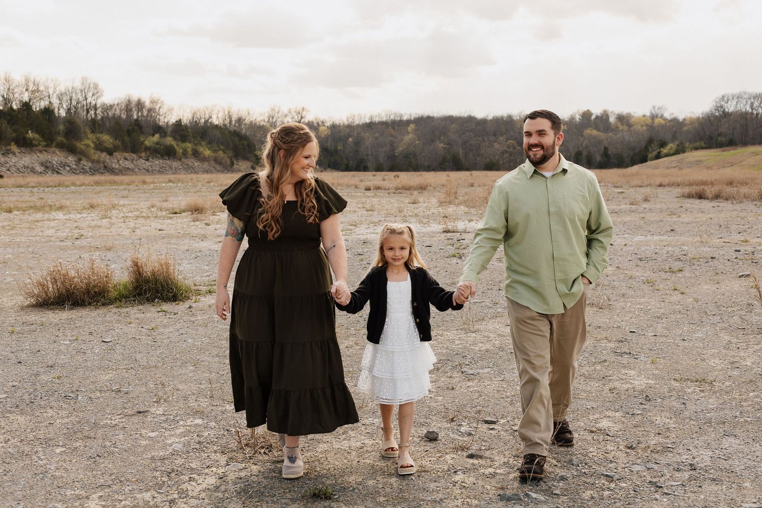 Family holds hands while walking together on rocky terrain with trees in background.