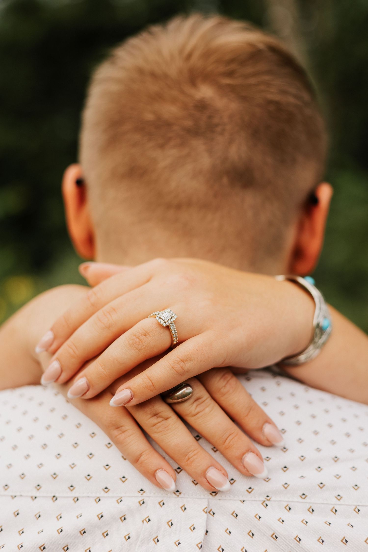 Close-up of engagement ring and hands resting on textured white fabric.