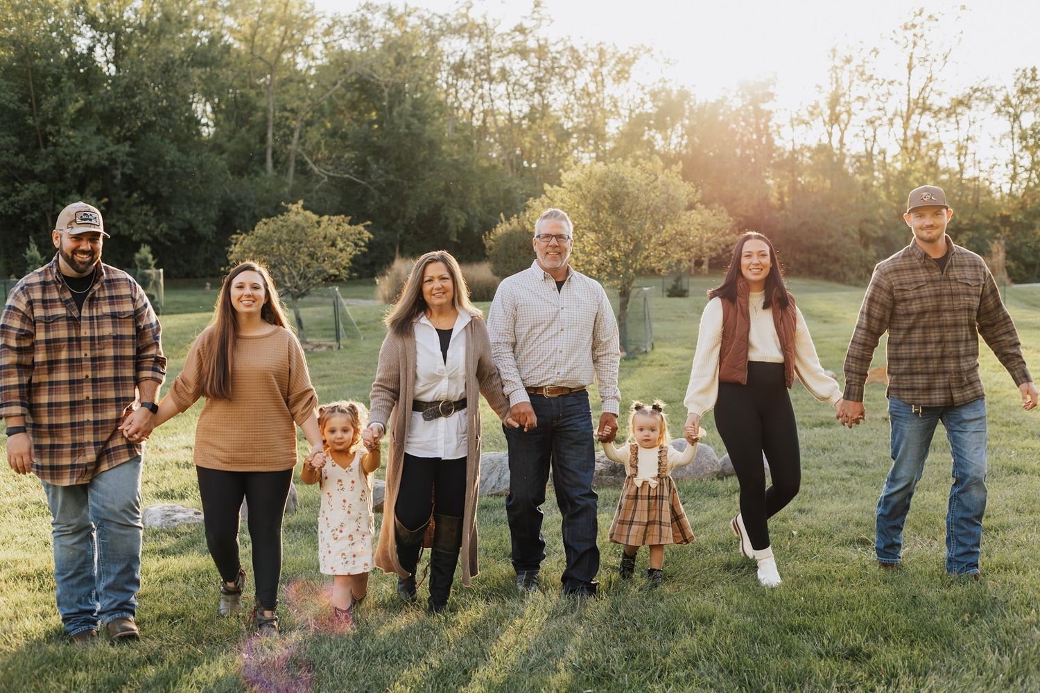 Extended family holding hands in a line outdoors during golden hour.