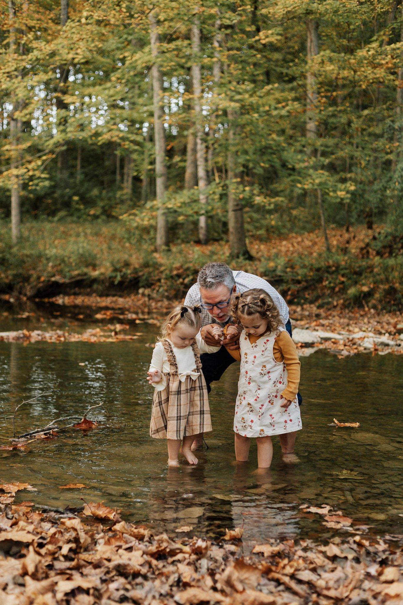 Children playing in shallow creek water surrounded by autumn leaves and forest.
