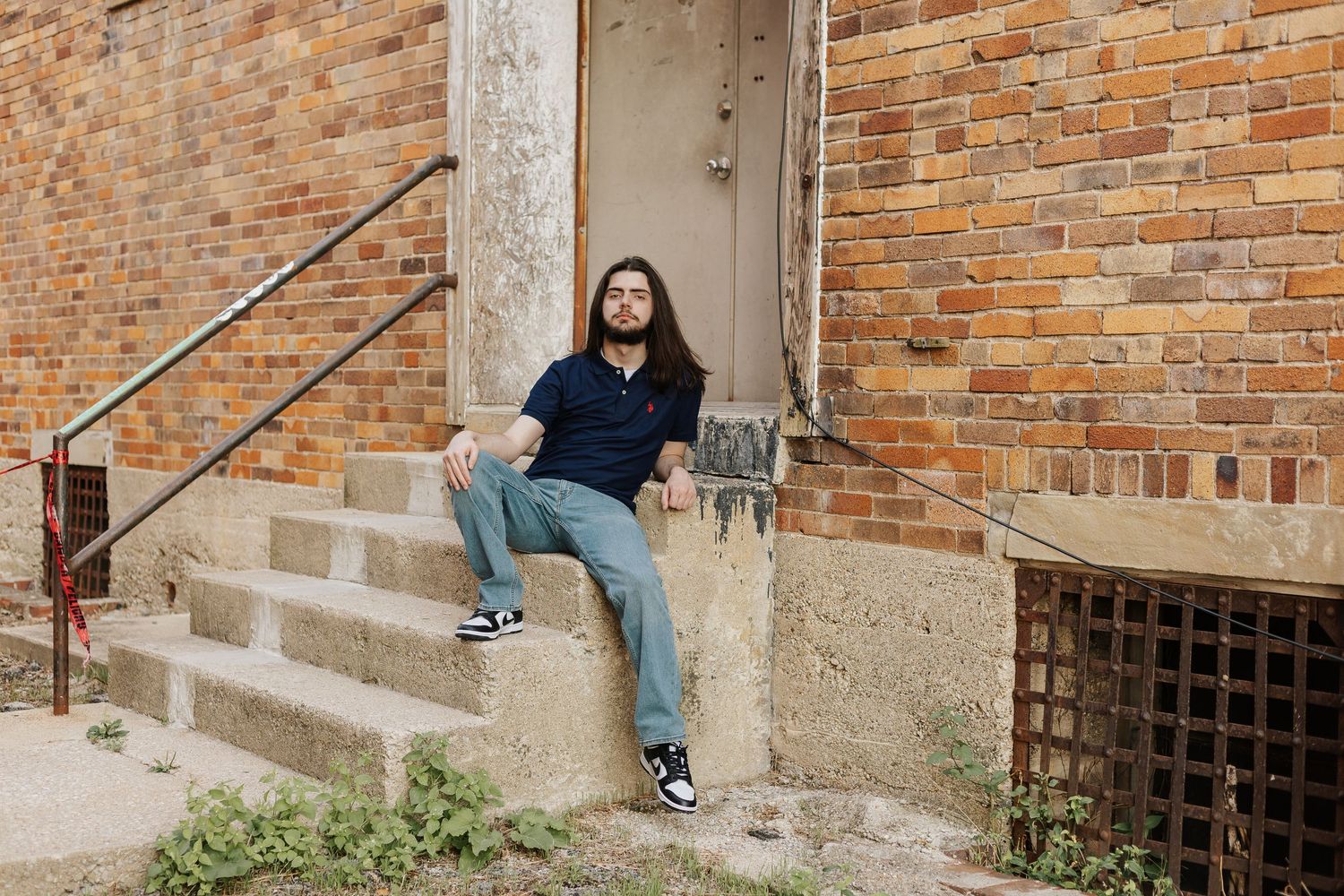 Person in casual wear sits on concrete steps by brick building.