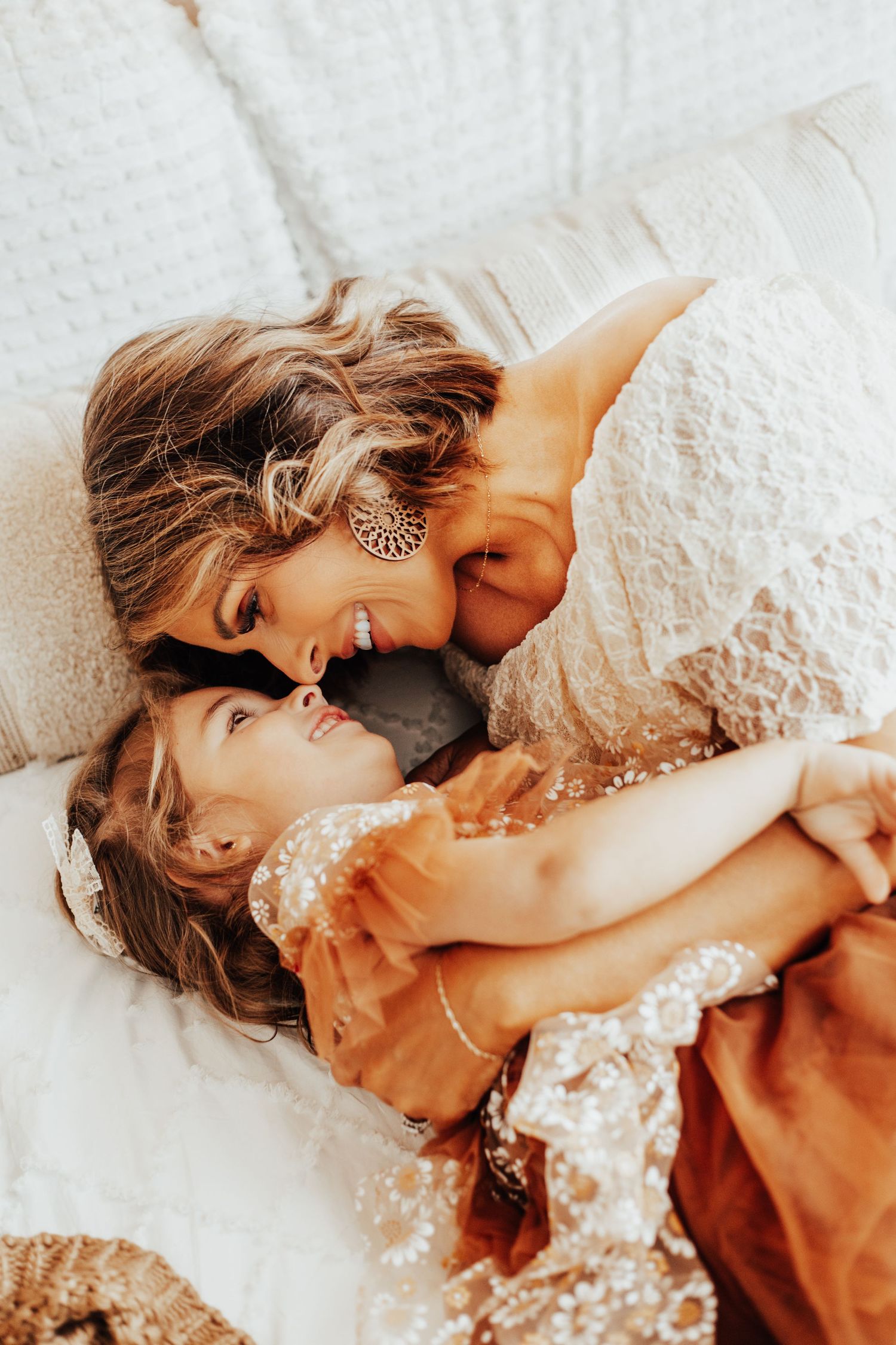 Tender moment between parent and child lying on white bedding in warm natural light.